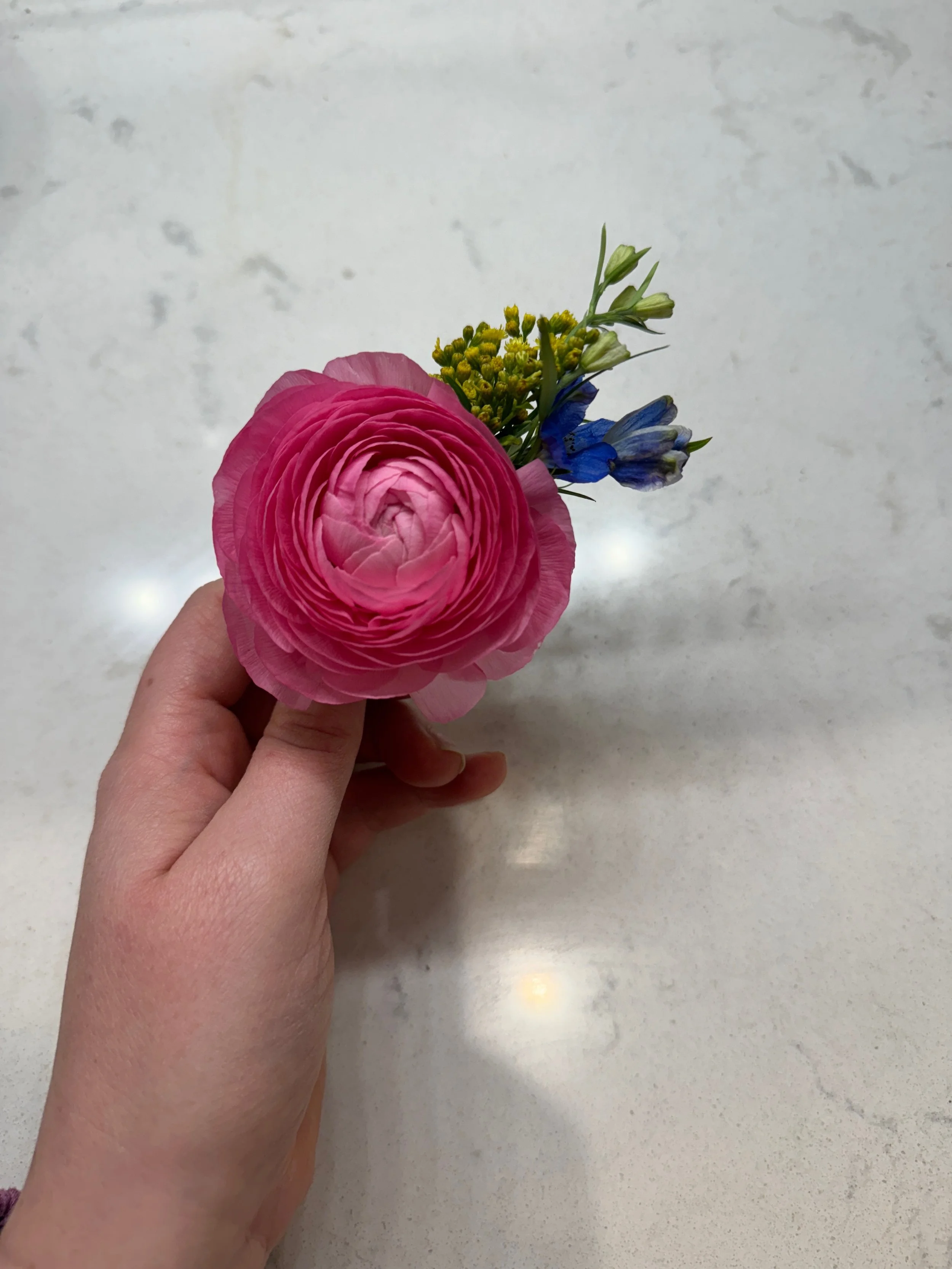 Person holding a small bouquet of pink, blue, and yellow flowers on a light granite surface.