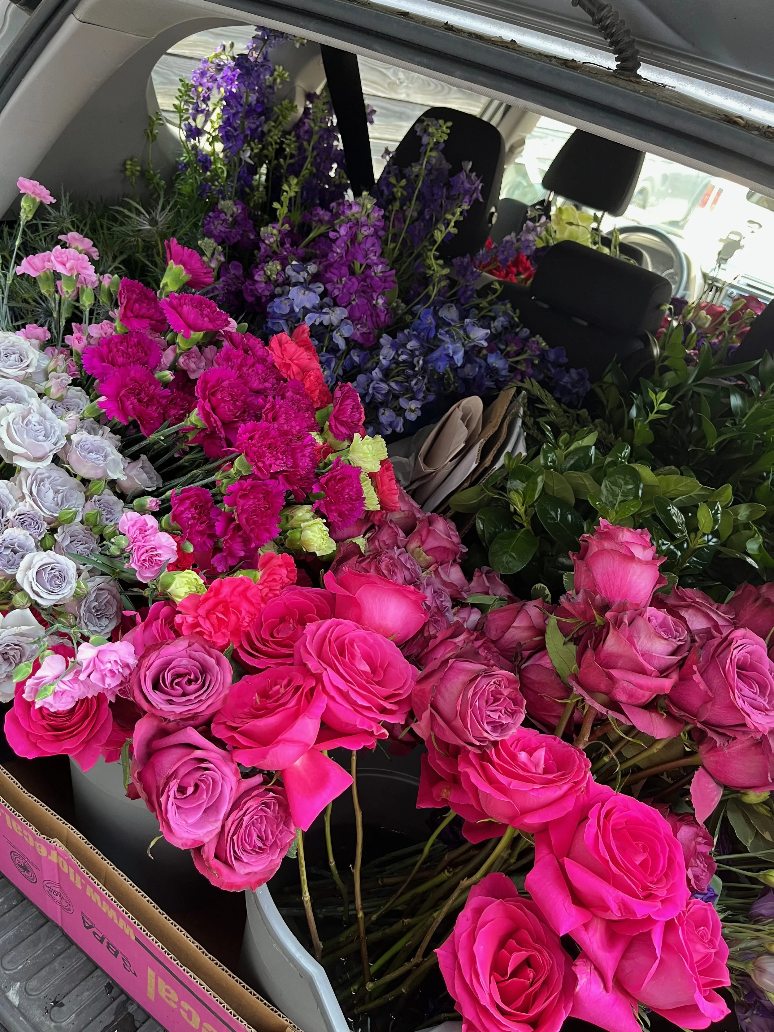 The trunk of a vehicle filled with various colorful flowers, including pink roses, purple irises, and other blooming flowers.