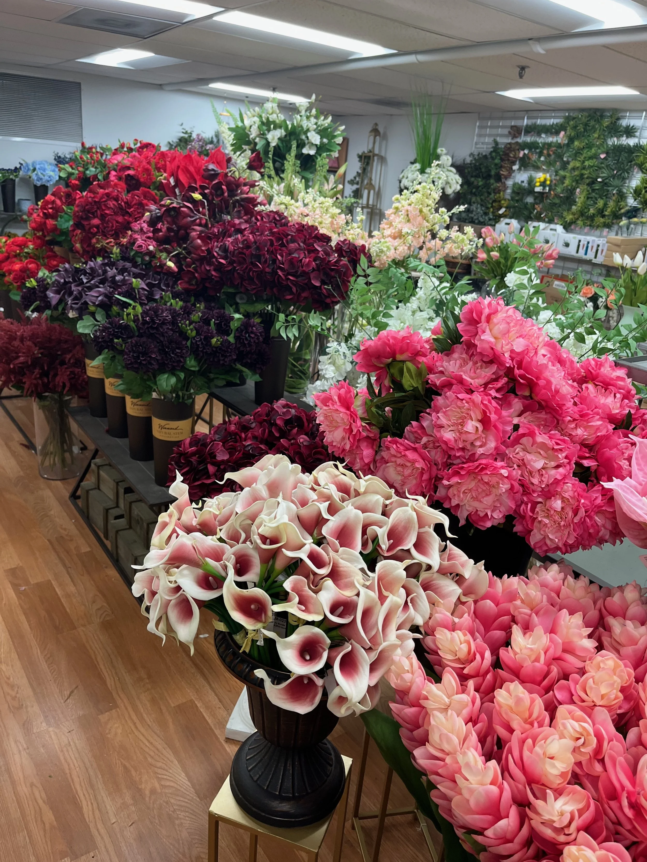 An indoor flower shop display with various colorful flowers including calla lilies, peonies, hydrangeas, and other blossoms.