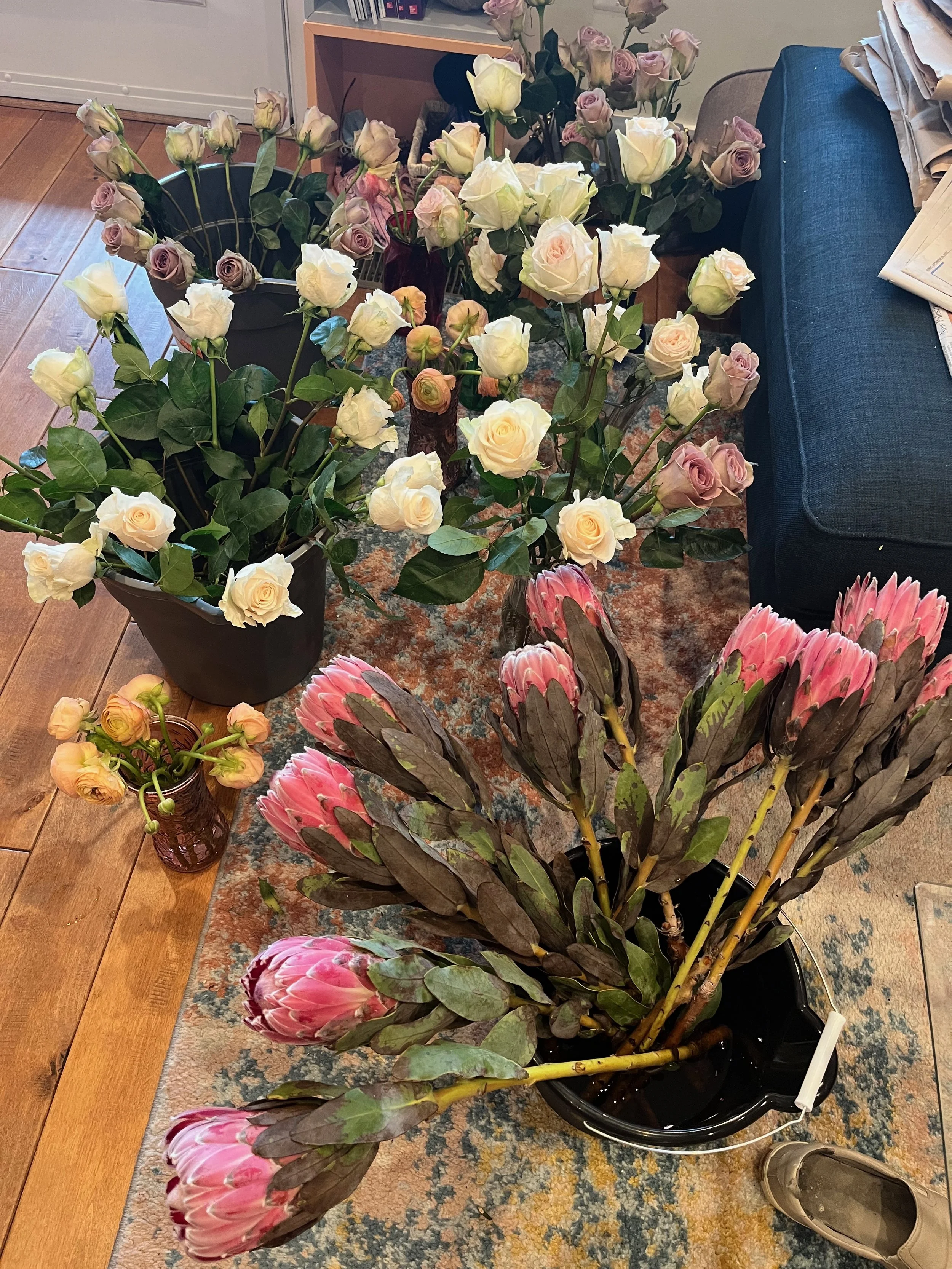 Various bouquets of roses in different colors, including white, pink, and lavender, arranged on a wooden table indoors.