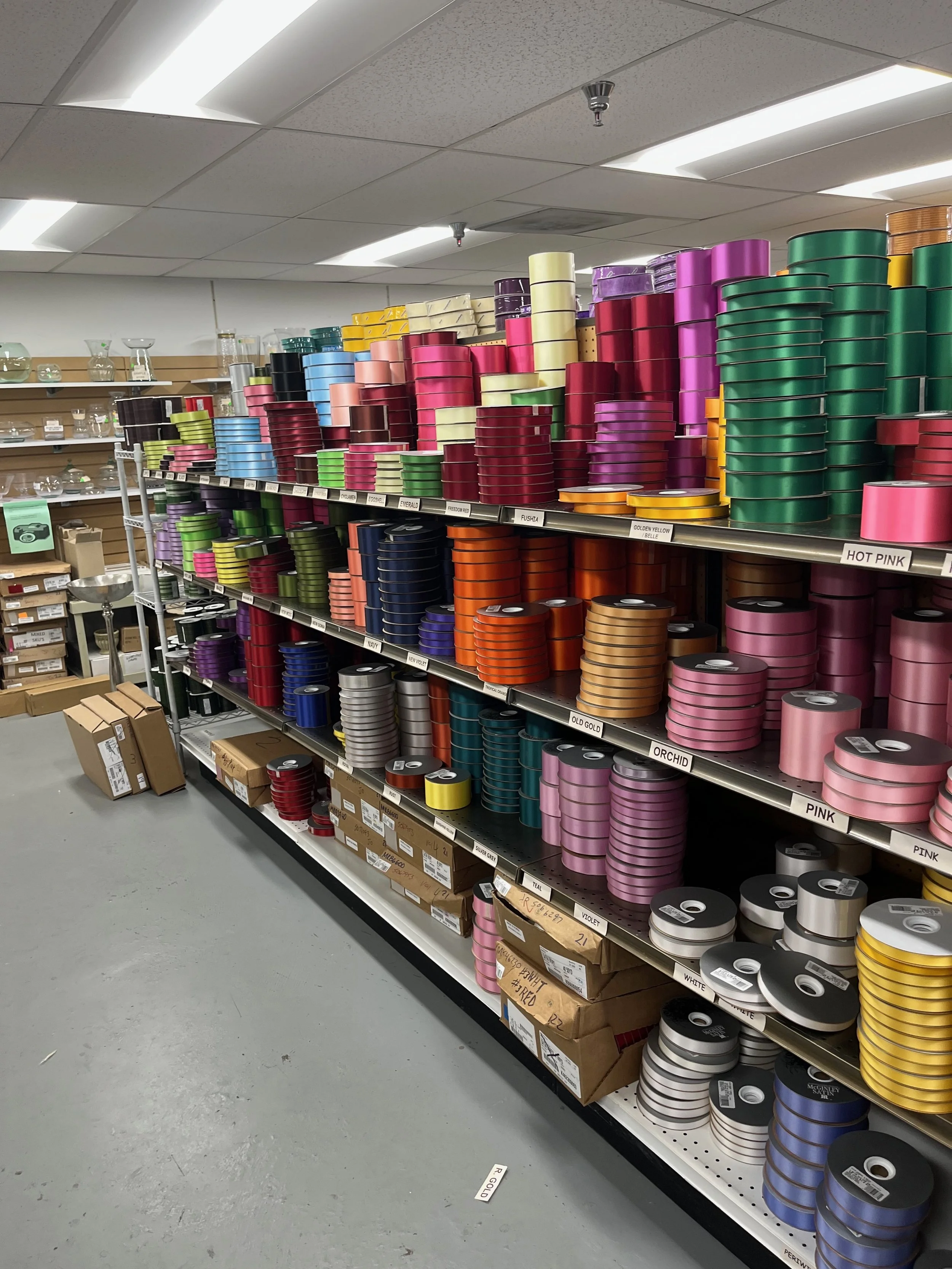Shelf with stacks of colorful ribbons in a store, arranged by color and size.
