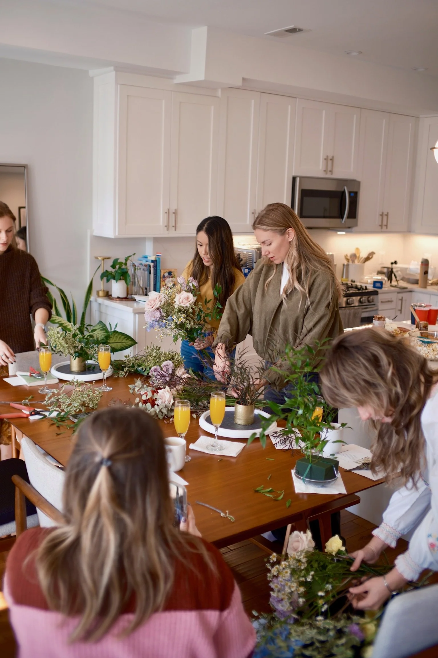 People arranging flowers on a dining table during a floral arrangement activity in a kitchen.