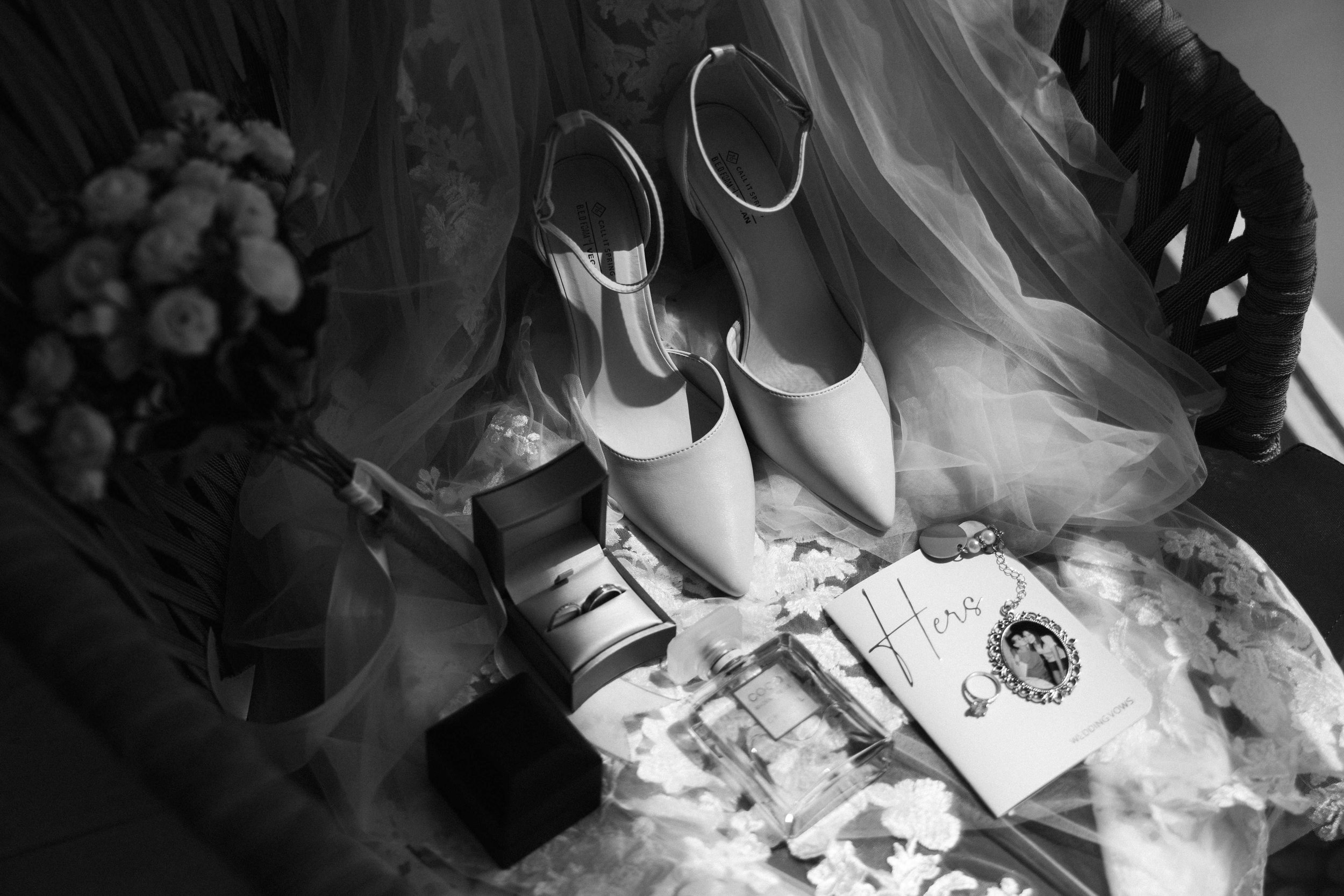 Wedding accessories: a pair of white high heels, a small video camera, a jewelry box with rings, a note card with 