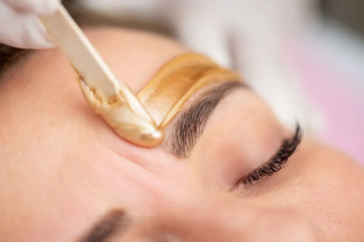 A person receiving an eyelash extension treatment with a brush applying adhesive on the eyelash area.