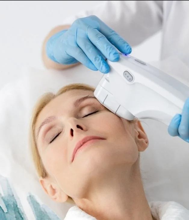 A healthcare professional using a handheld device on a woman's forehead during a medical procedure.