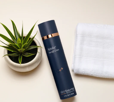 A potted plant, a bottle of skin care product, and a folded white towel on a white surface.