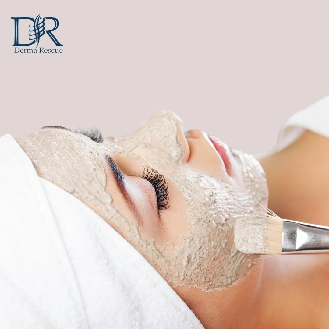 A woman with closed eyes receiving a facial treatment with a clay mask applied to her face, lying down with a white towel or headband, in a spa or skincare clinic.