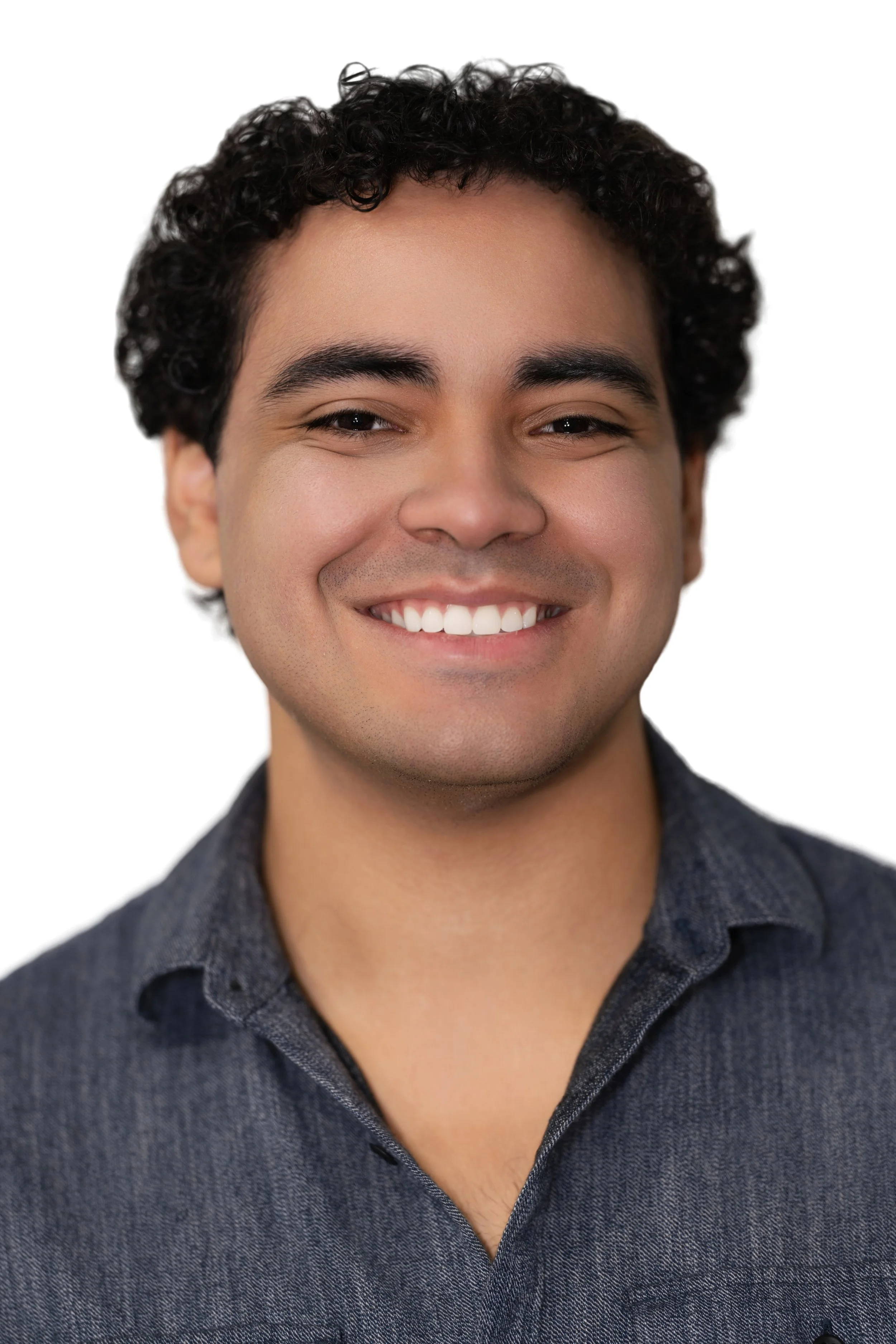 A smiling young man with curly dark hair wearing a dark collared shirt against a plain white background.