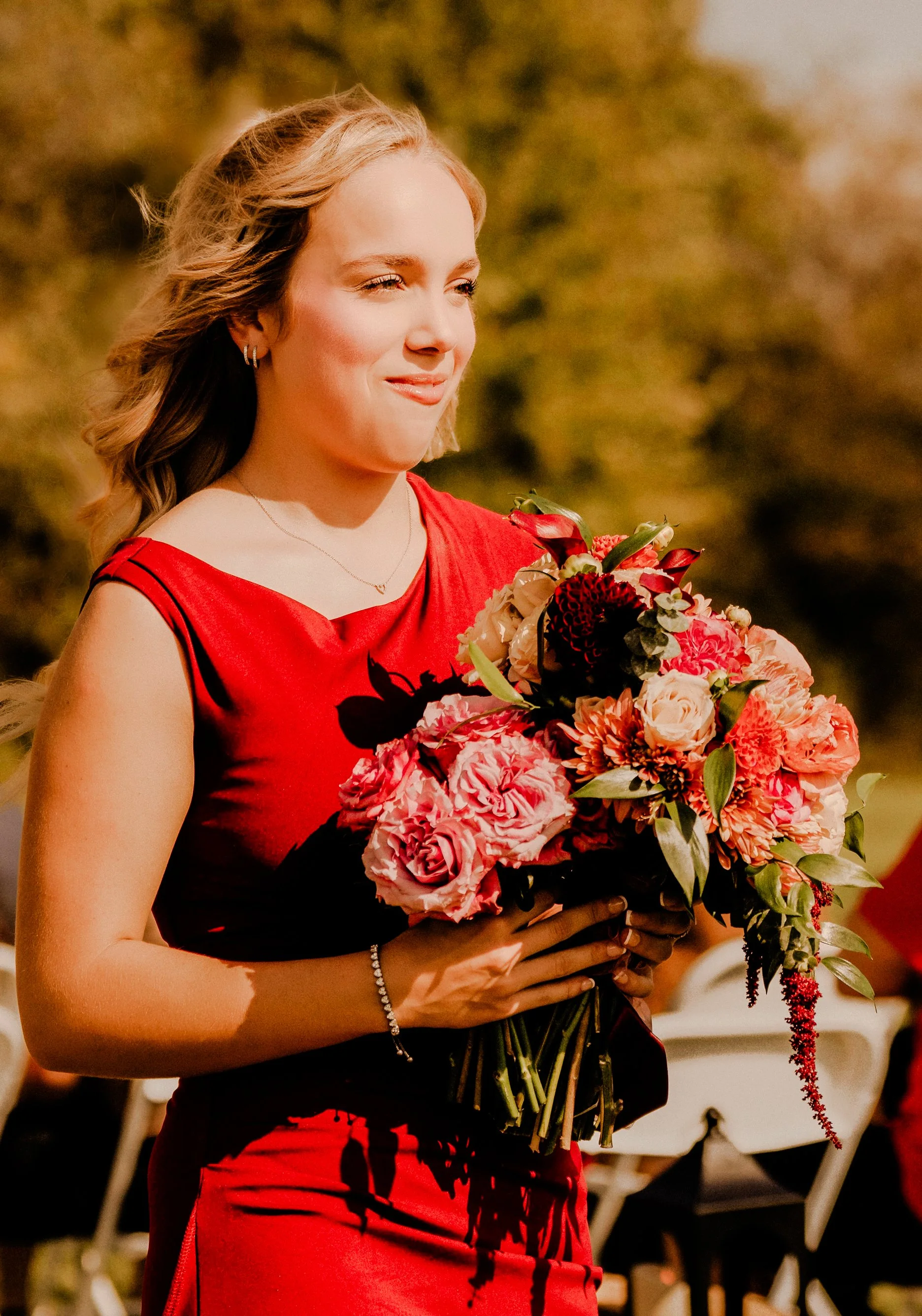 A woman in a red dress holding a bouquet of pink, red, and white flowers outdoors during daytime.