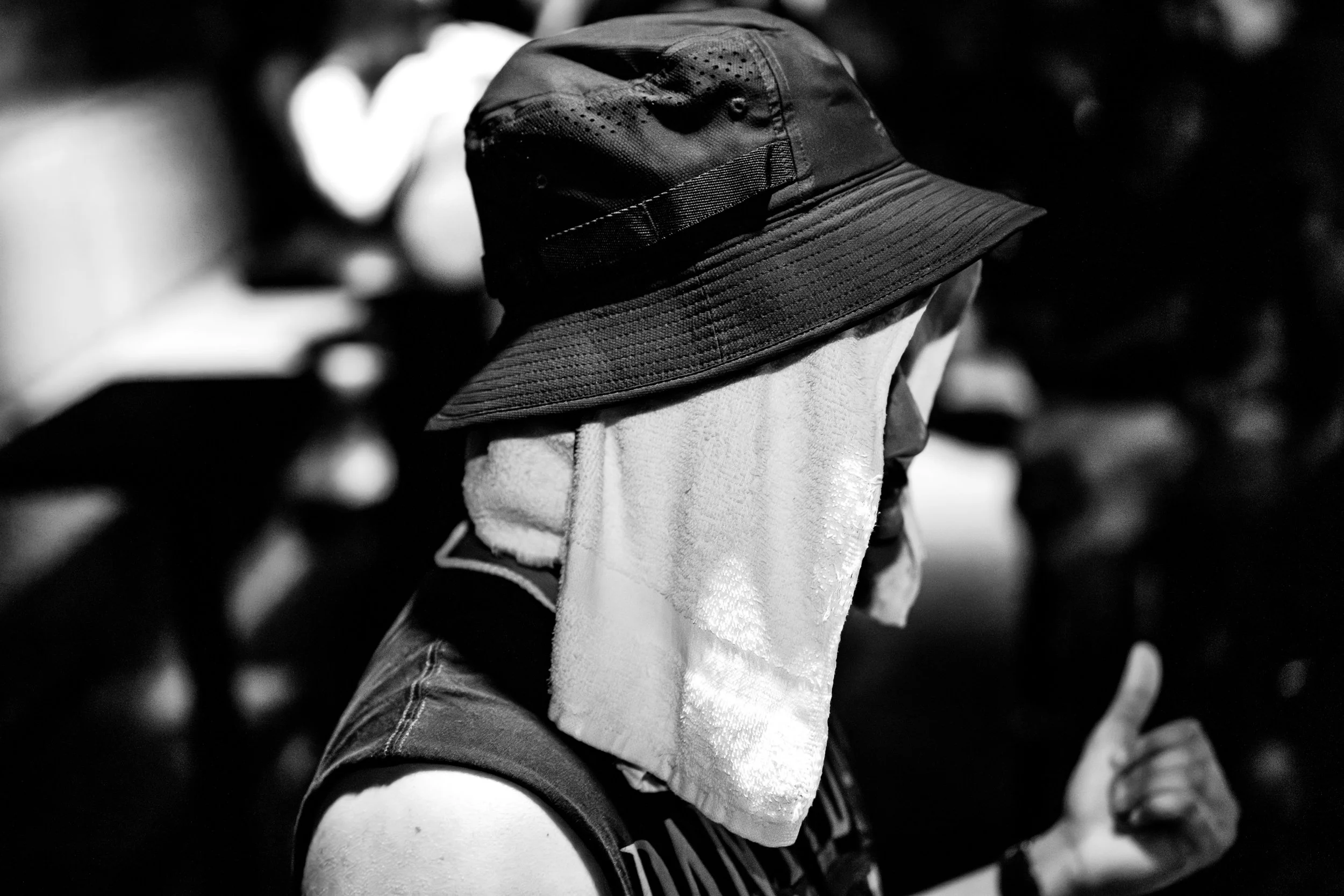 A person wearing a bucket hat with a towel draped over their face, giving a thumbs-up gesture.