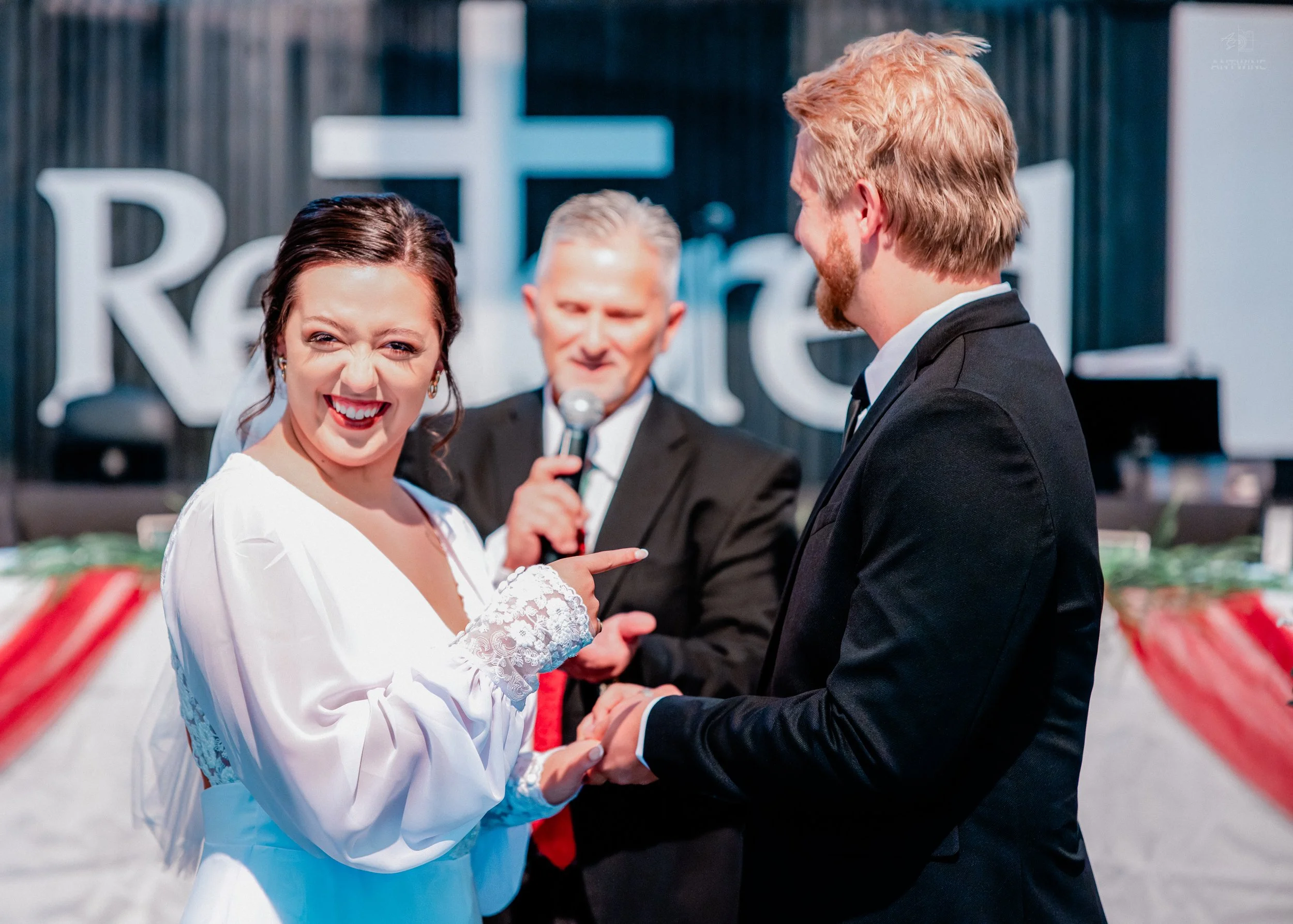 A bride and groom exchanging wedding vows during a ceremony, with an officiant in the background.