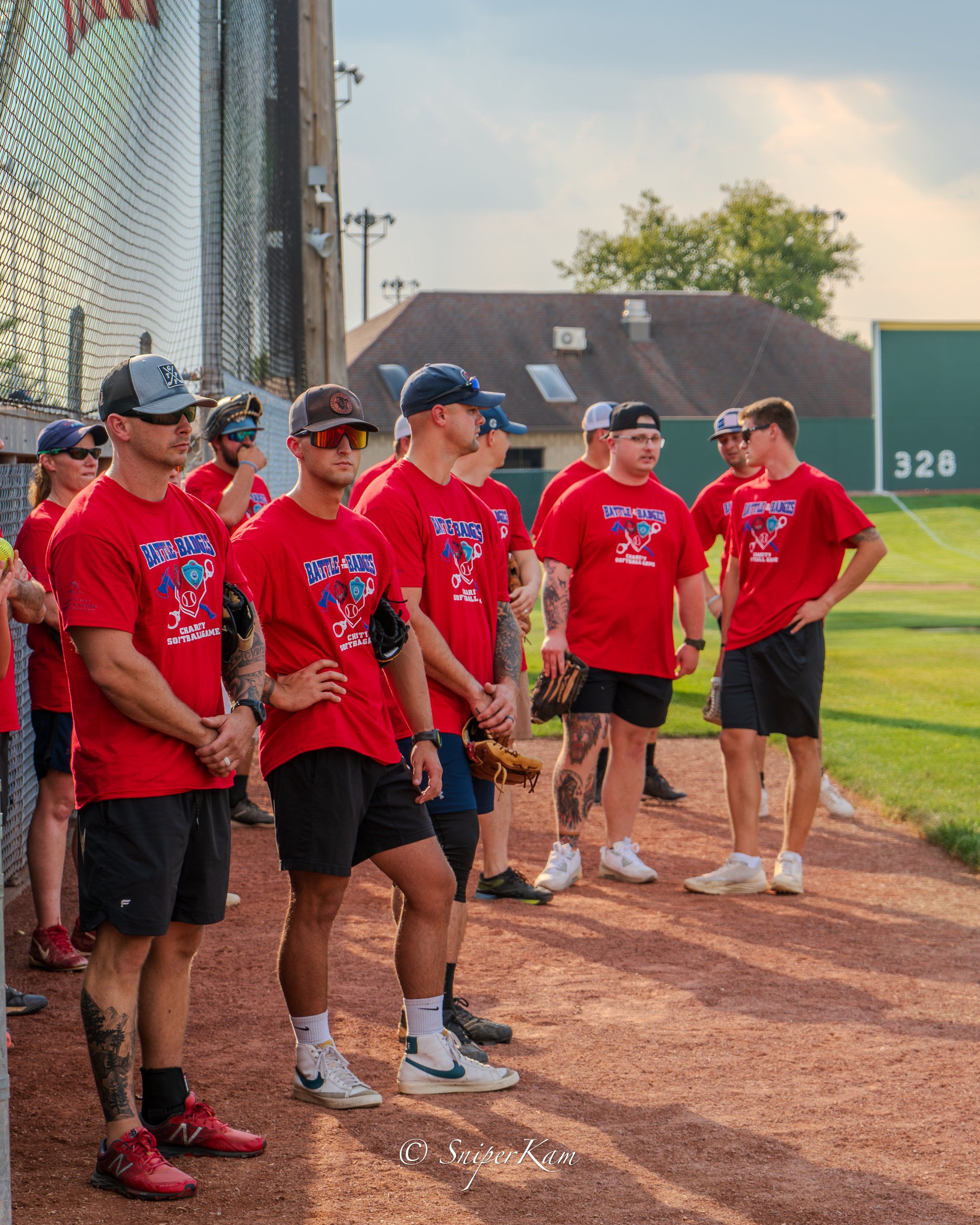 Group of baseball players standing on the field during a game, wearing red shirts and casual athletic clothing.
