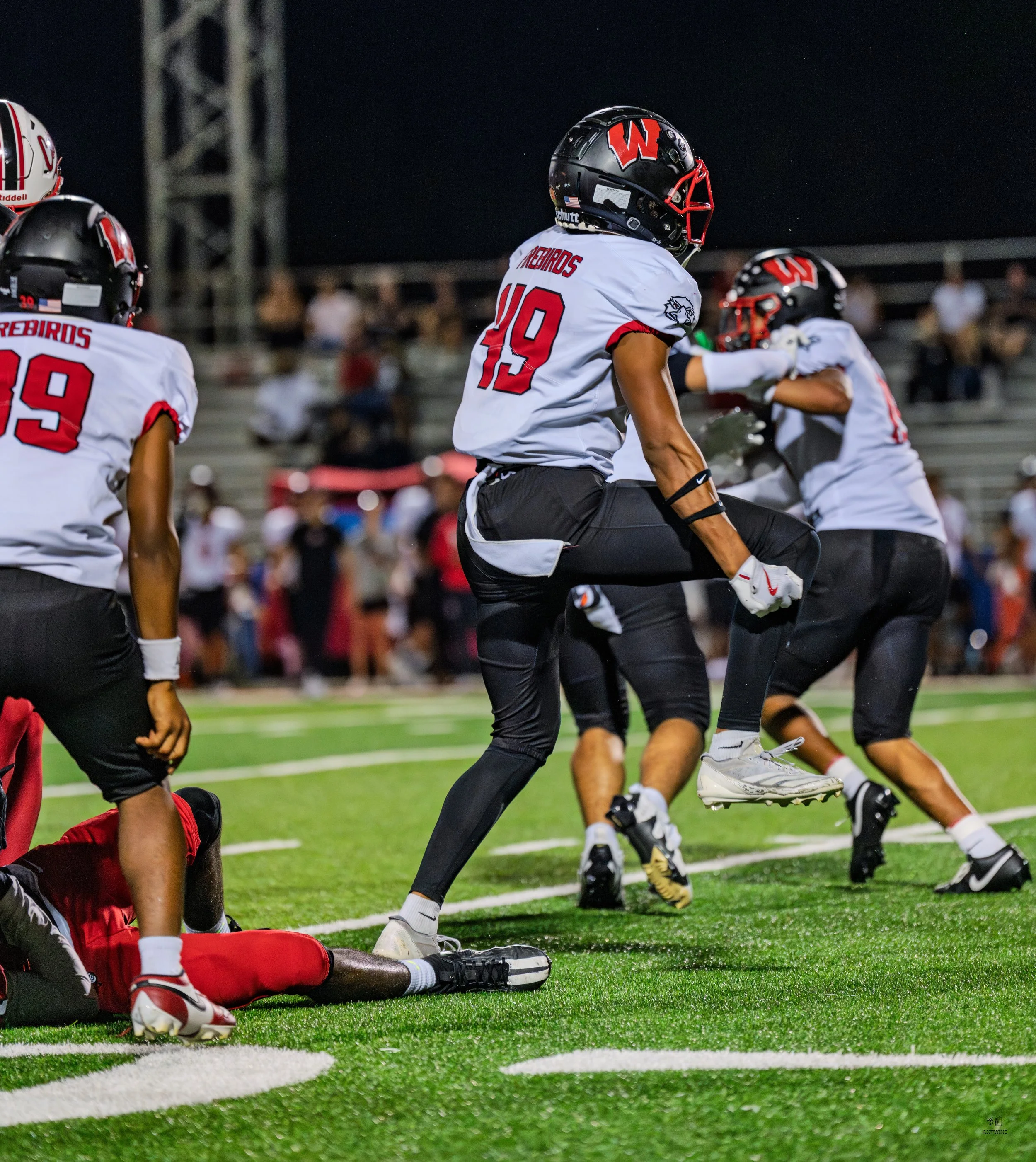 Football players in uniforms celebrating on the field at night, with one player mid-air jumping.