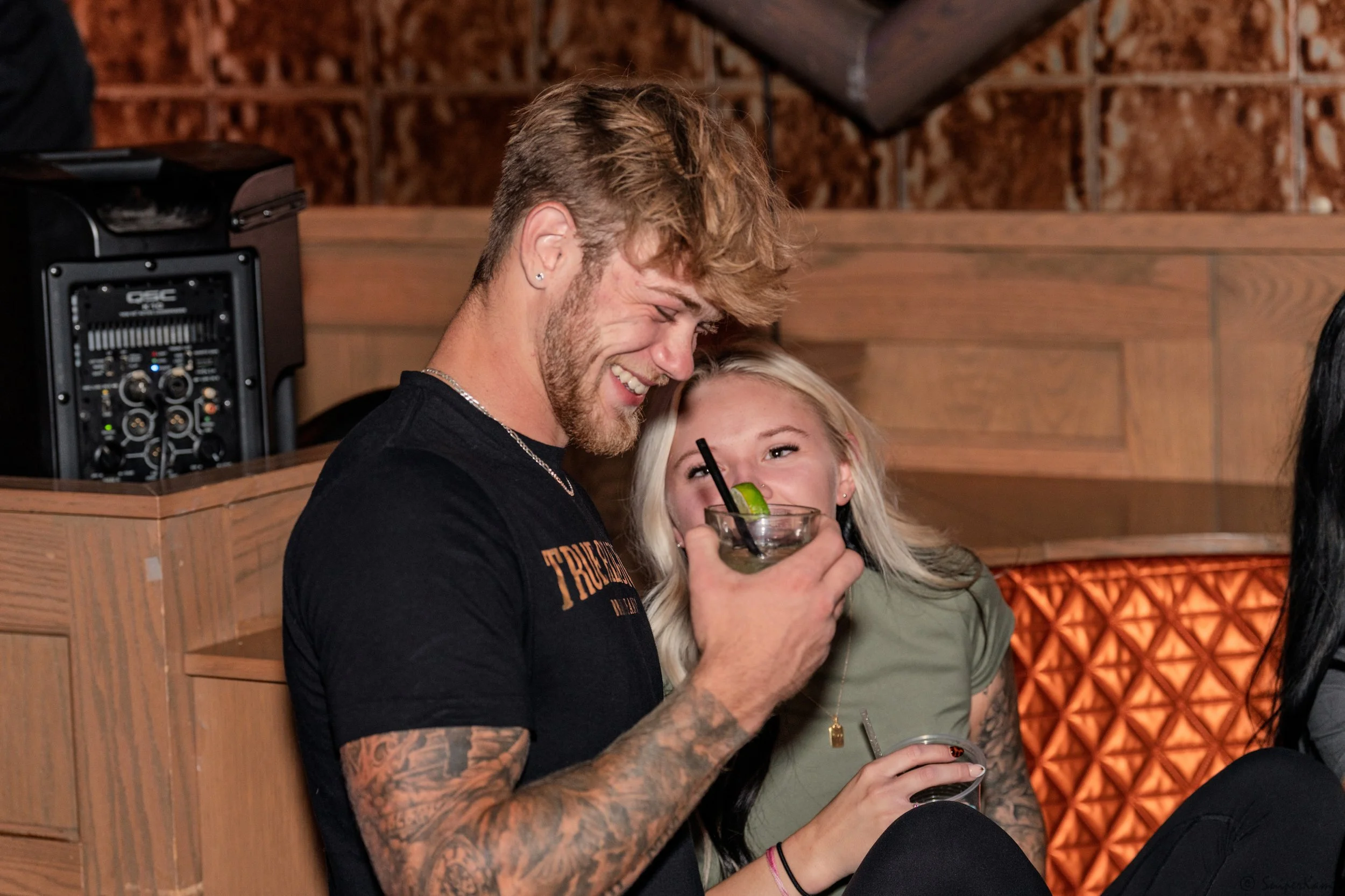 A young man and woman sharing a drink and laughing together in a lively bar setting.