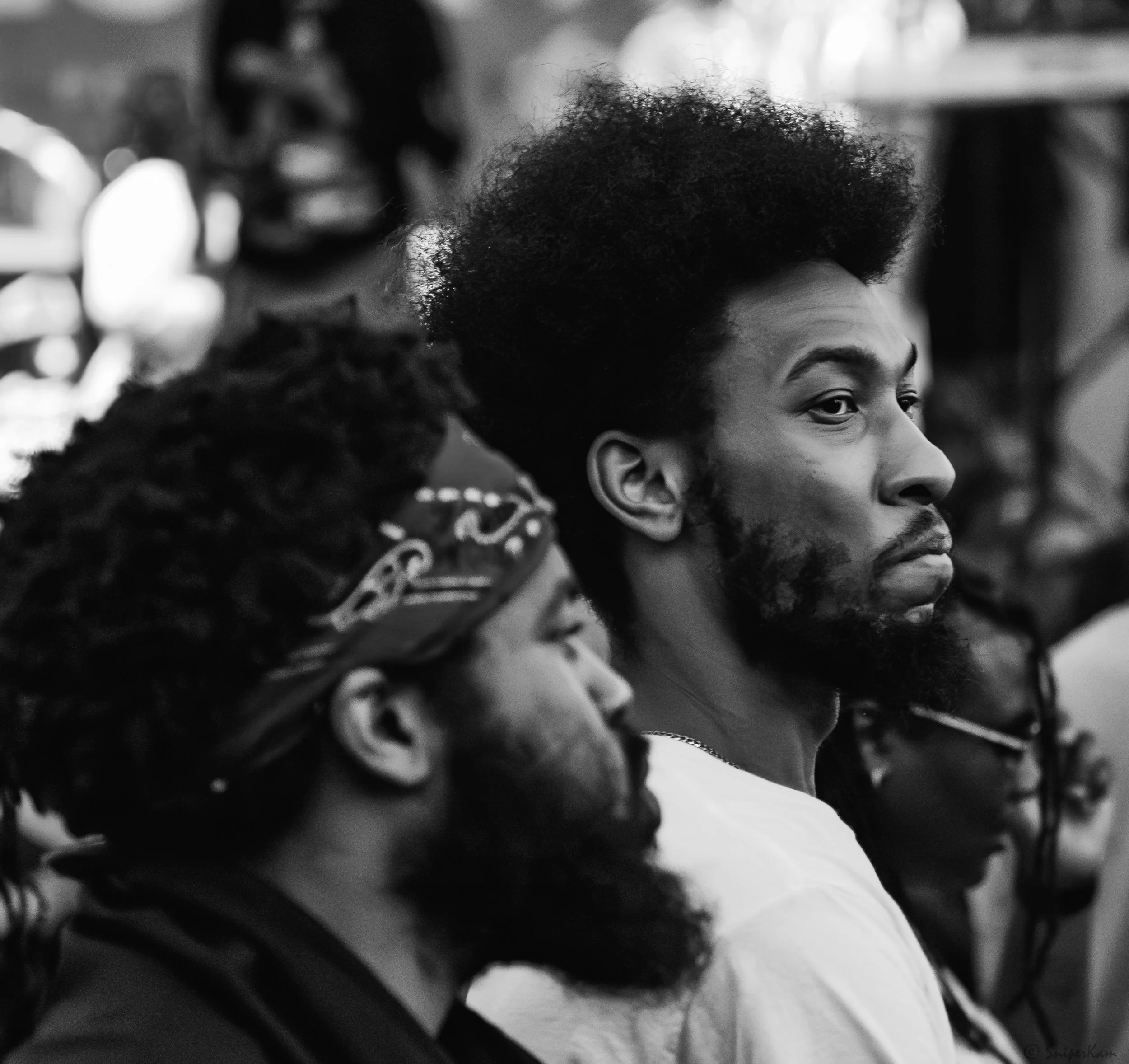 Three men with beards and hairstyles, sitting and looking to the right, in a black and white photo.