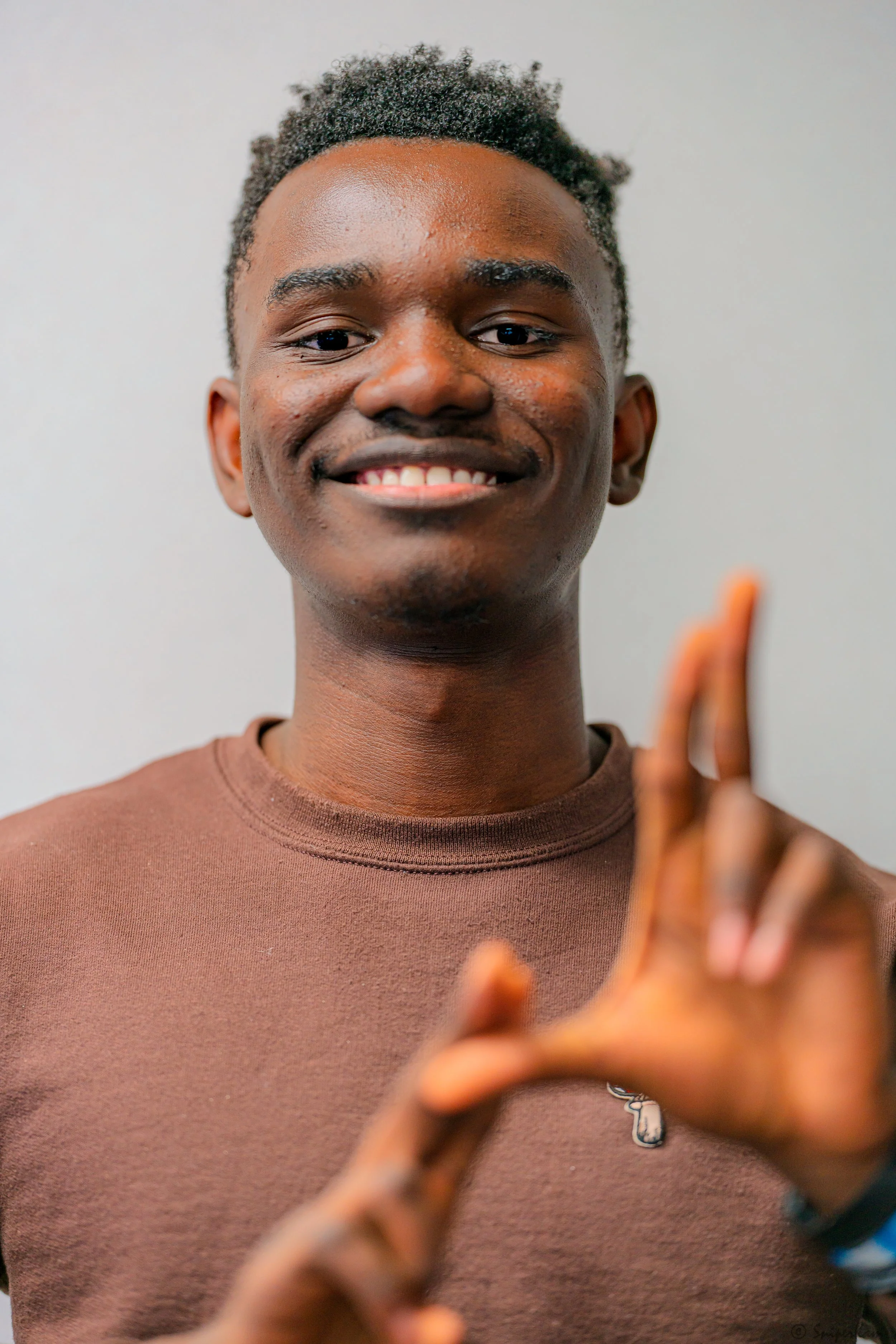 A young man smiling at the camera, making a gesture with his hand.