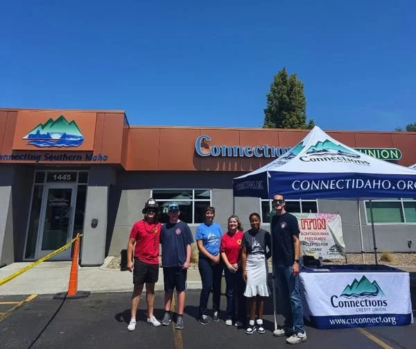 Group of six people standing outside a building with a Connect Idaho sign, a canopy with Connect Idaho branding, and orange traffic cones in the parking lot.