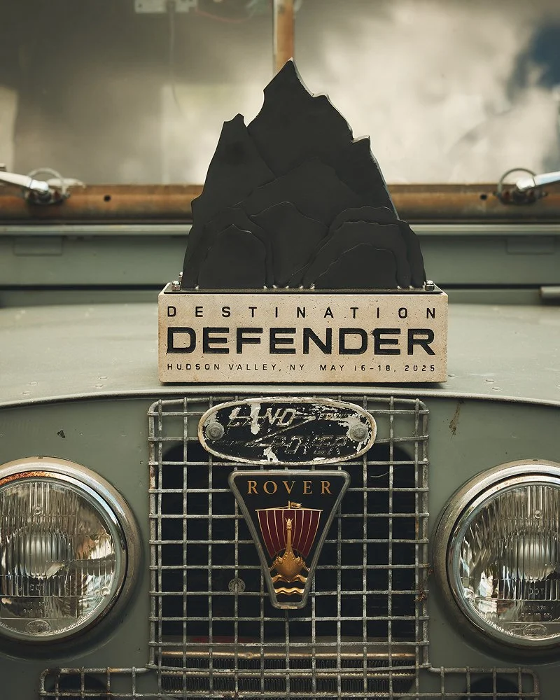 Close-up of a vintage Rover vehicle's front with a rally plate on top advertising the Destination DEFENDER event in Hudson Valley, NY, May 16-18, 2025.