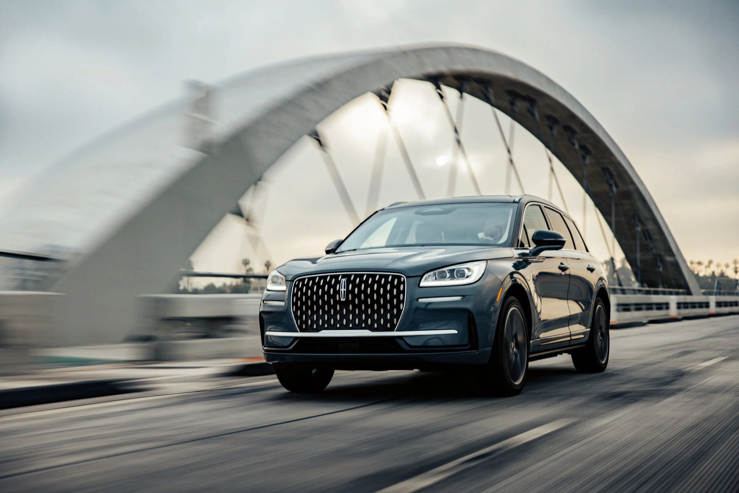 A sleek black luxury SUV driving on a bridge with a large white arch structure in the background.