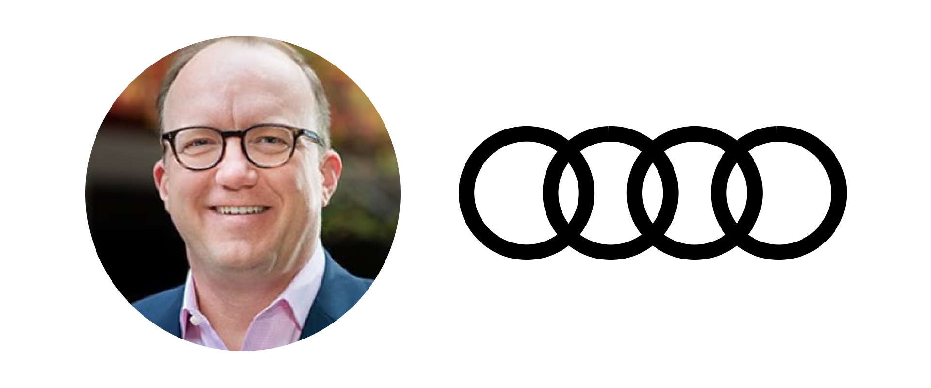 A smiling man with glasses wearing a suit and pink shirt outdoor with blurred greenery background.