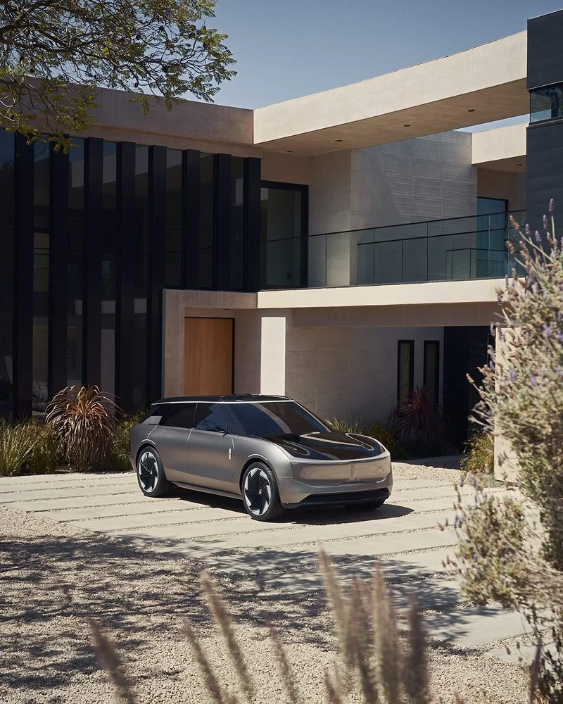 A modern, sleek electric car parked in front of a contemporary house with large windows, a glass balcony, and minimalist architecture.