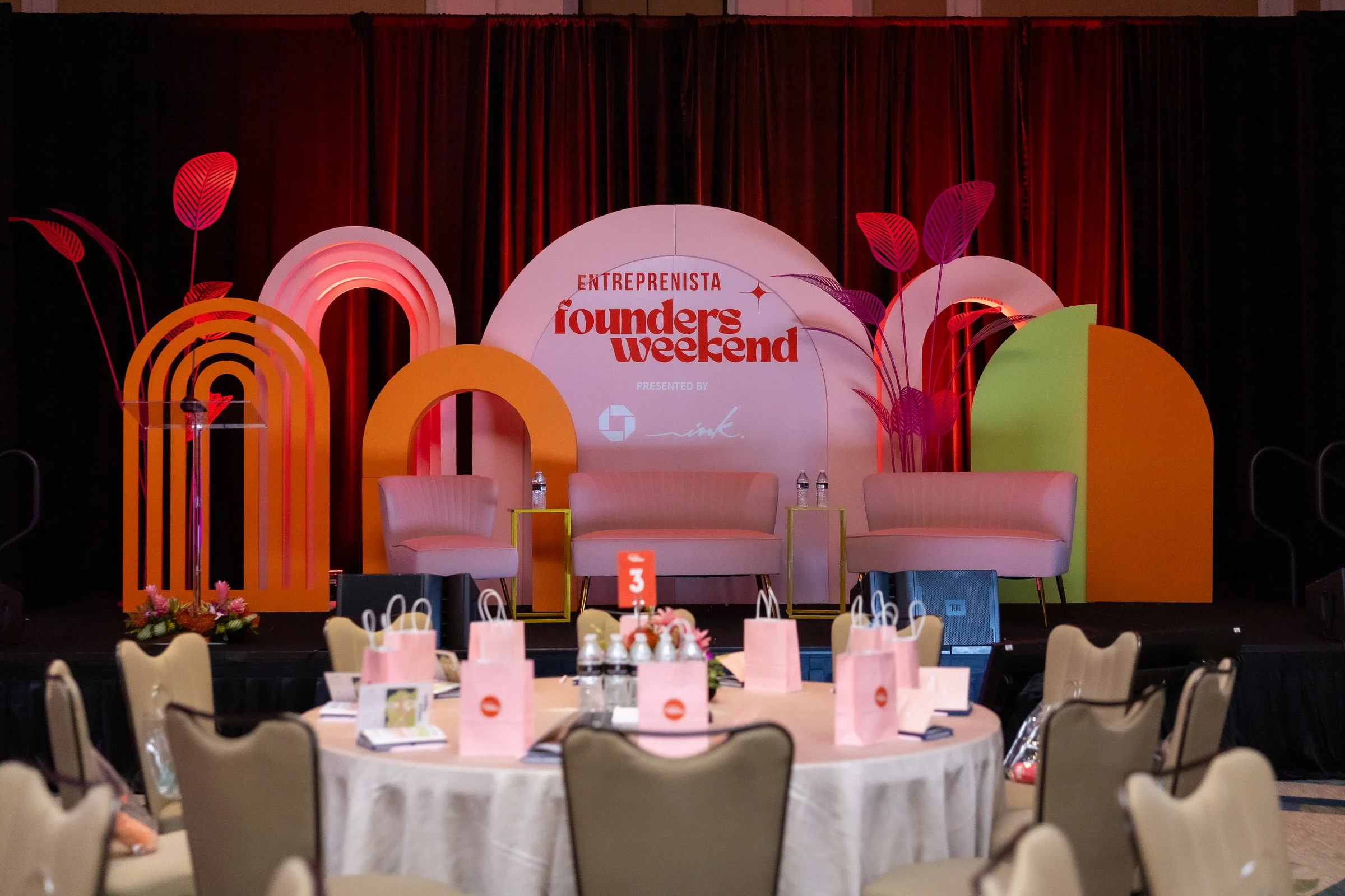 Stage setup for Entrepreneurs Weekend event with colorful abstract decorations, chairs, tables with gift bags, and a large central backdrop displaying the event name.