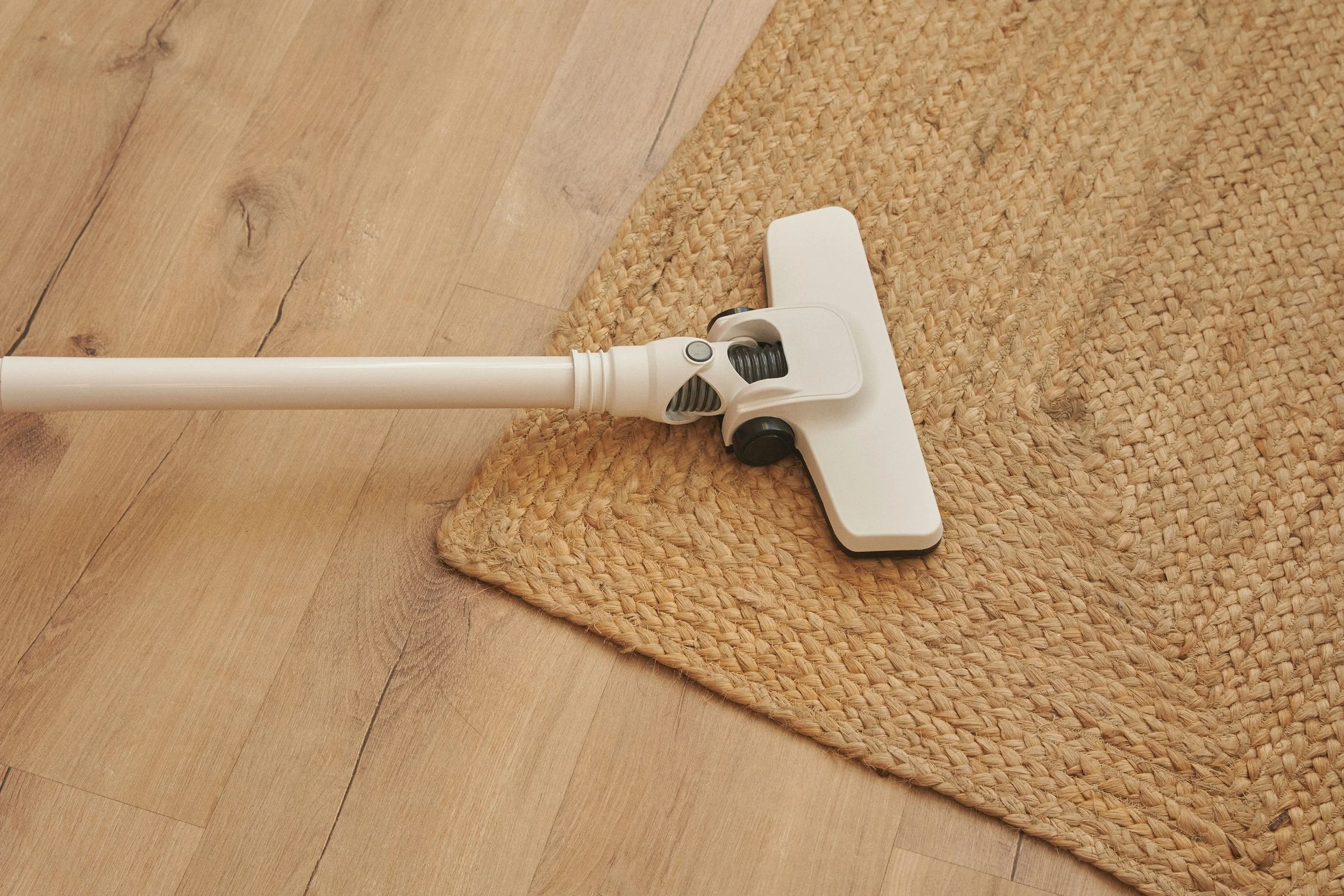 A white vacuum cleaner head on a woven area rug, with wood floor visible nearby.