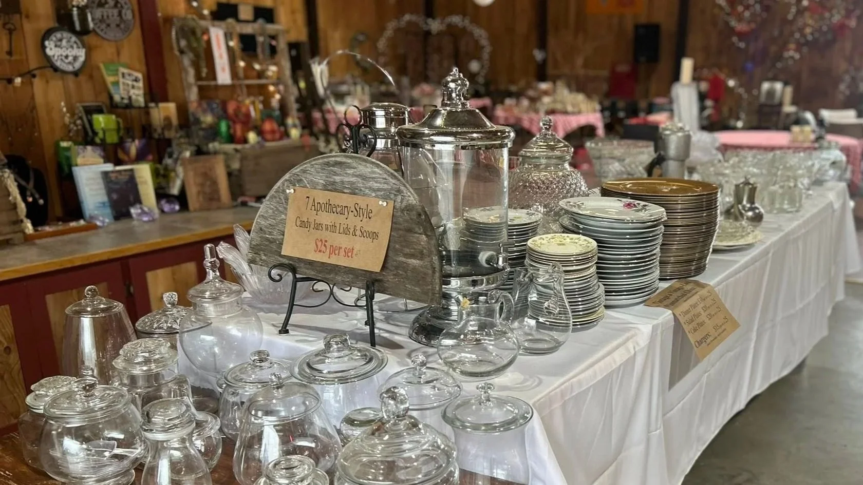 Table filled with vintage glass candy jars, plates, and bowls at a thrift or antique store.