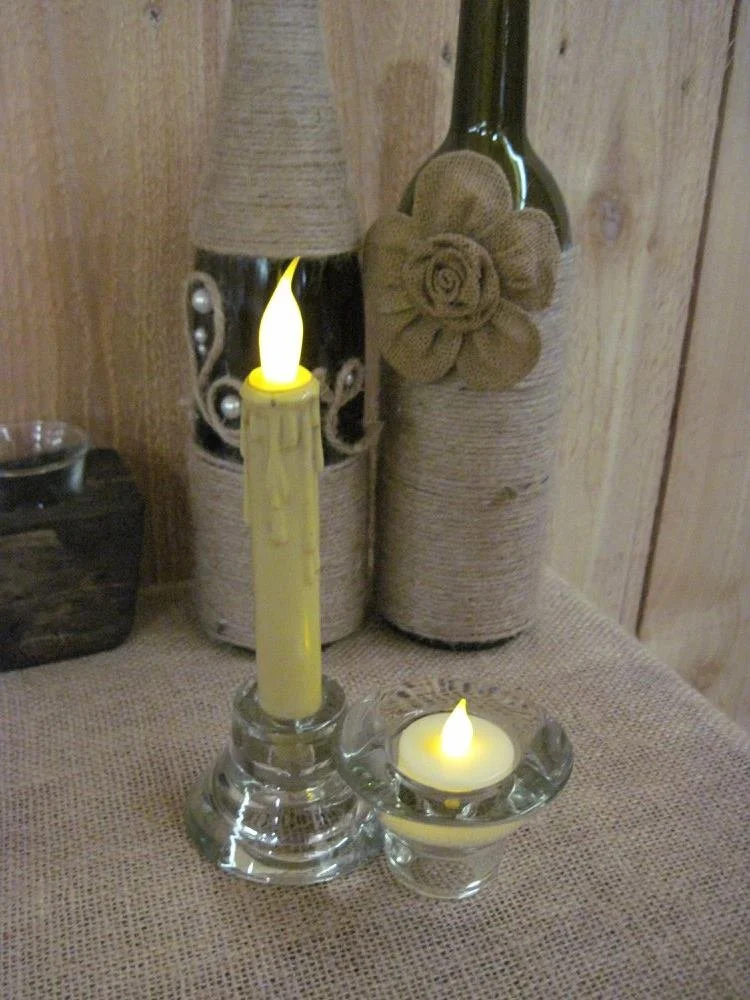 Vase with a faux candle flame, a tealight with a faux flame, and decorative bottles wrapped with burlap and twine, placed on a textured surface against a wooden background.