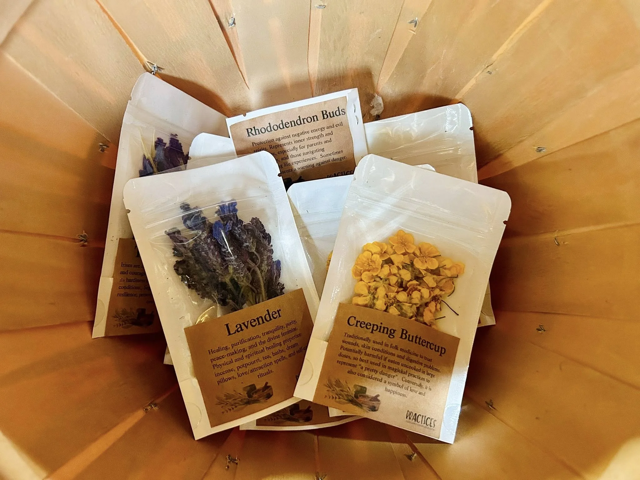 Three small bags of dried herbs inside a wooden container. The herbs are labeled lavender, creeping buttercup, and rhododendron buds.