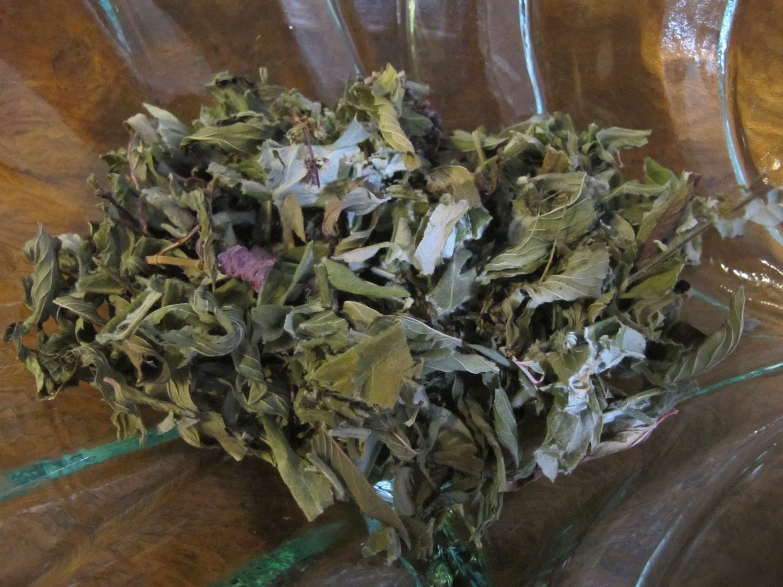 Dried herbs in a glass bowl on a wooden surface.