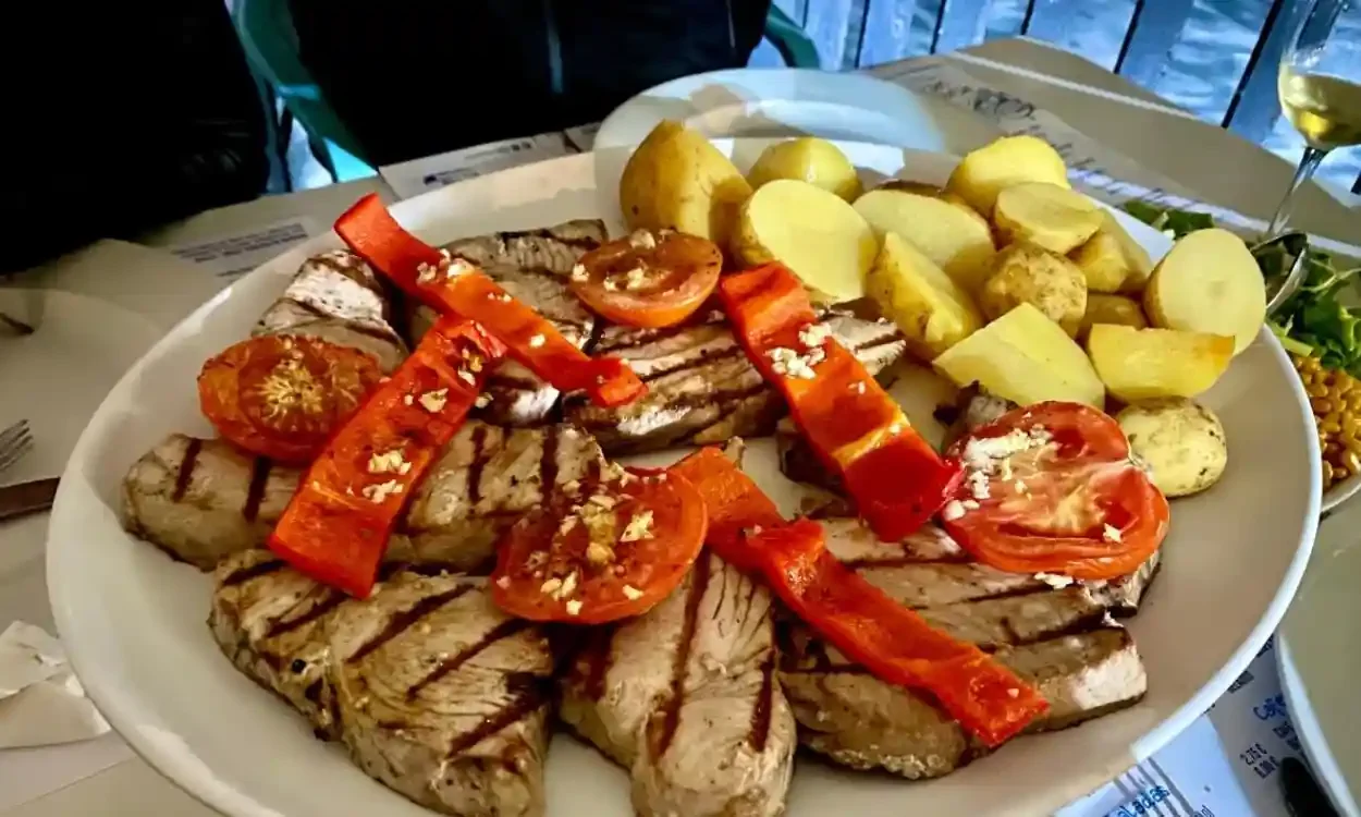 Grilled steak with grilled red peppers and tomatoes, boiled potatoes, and a glass of white wine on a white plate.