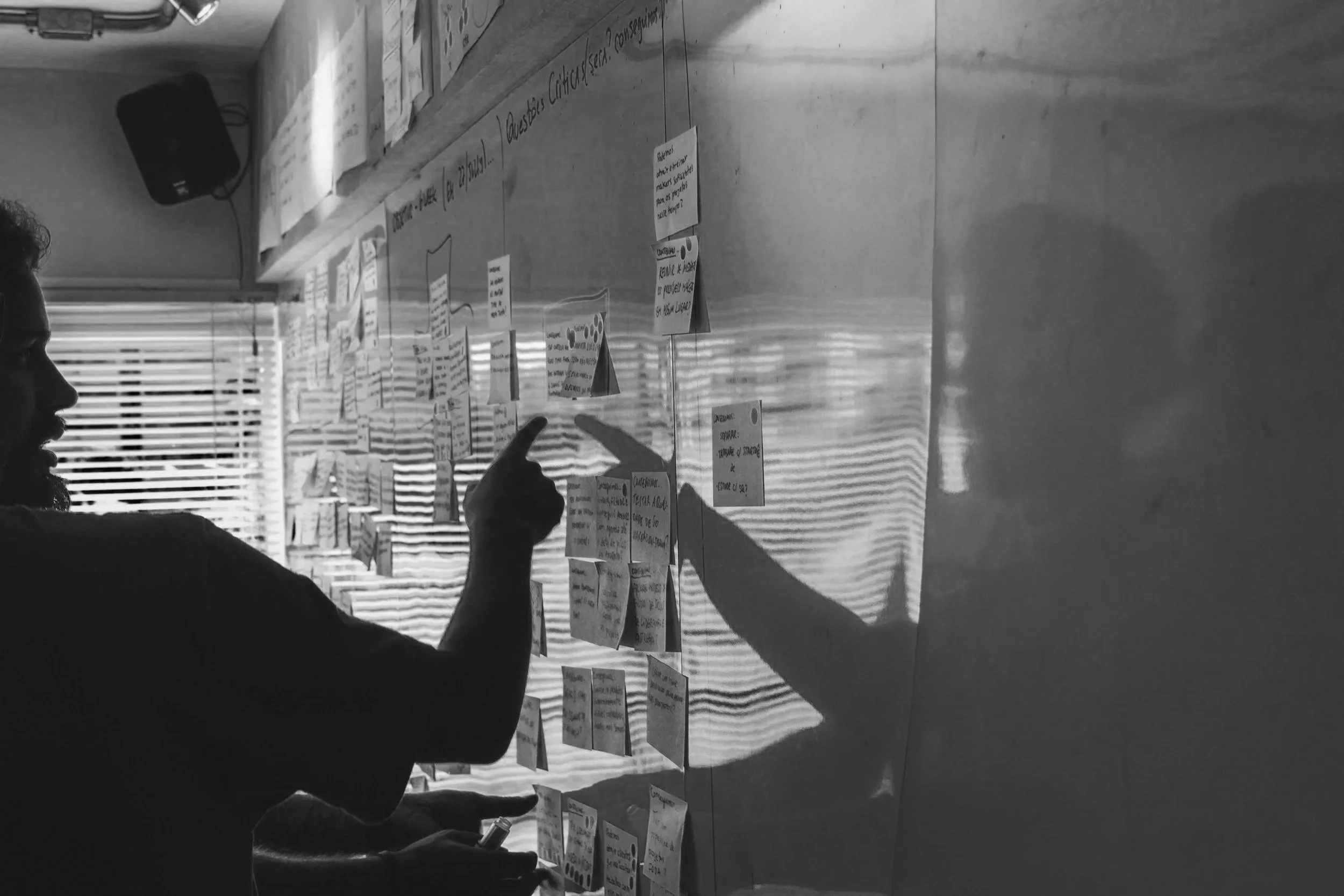 Person pointing at sticky notes on a wall with shadows cast from window blinds.