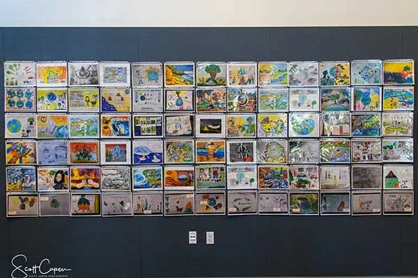 A wall display of numerous colorful children's drawings arranged in a grid, with a dark blue stripe at the top and bottom of the wall.
