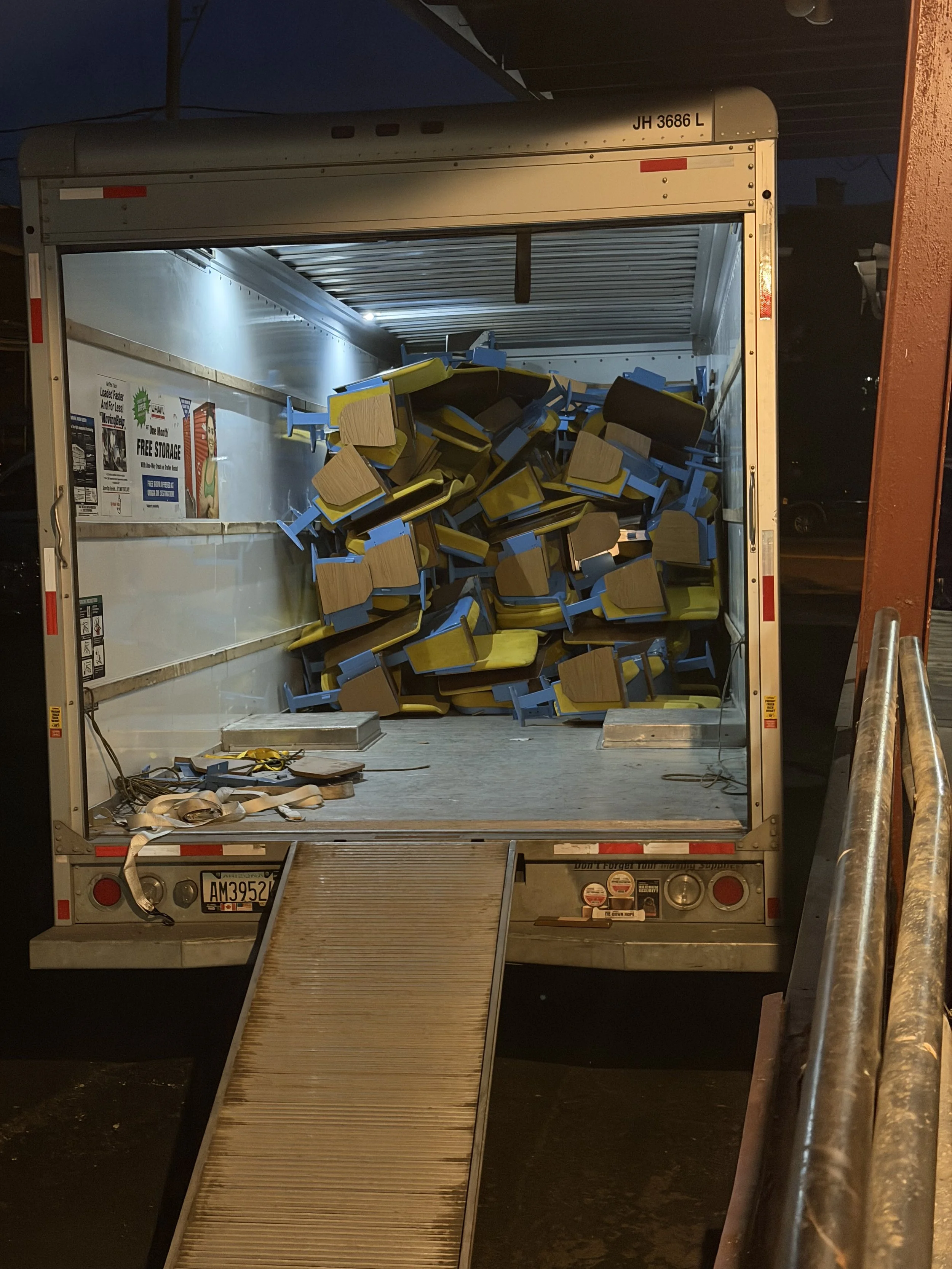 The back of a delivery truck filled with overturned chairs, some on the ground, at night.