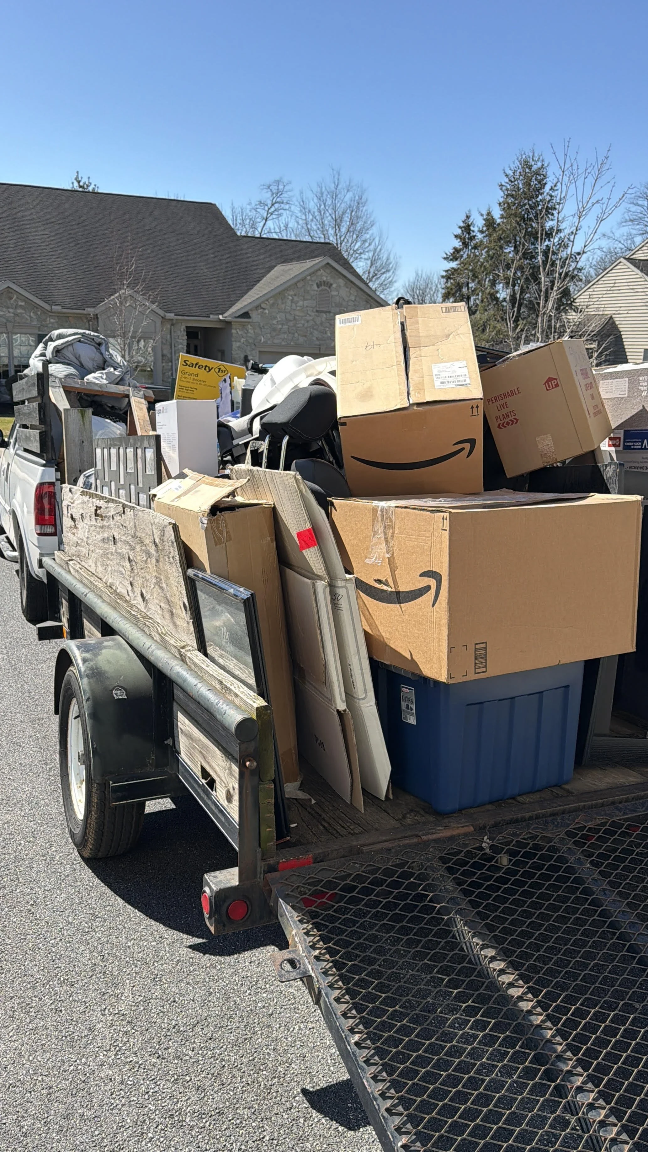 A trailer loaded with various household items, cardboard boxes, and furniture parked on a residential street.