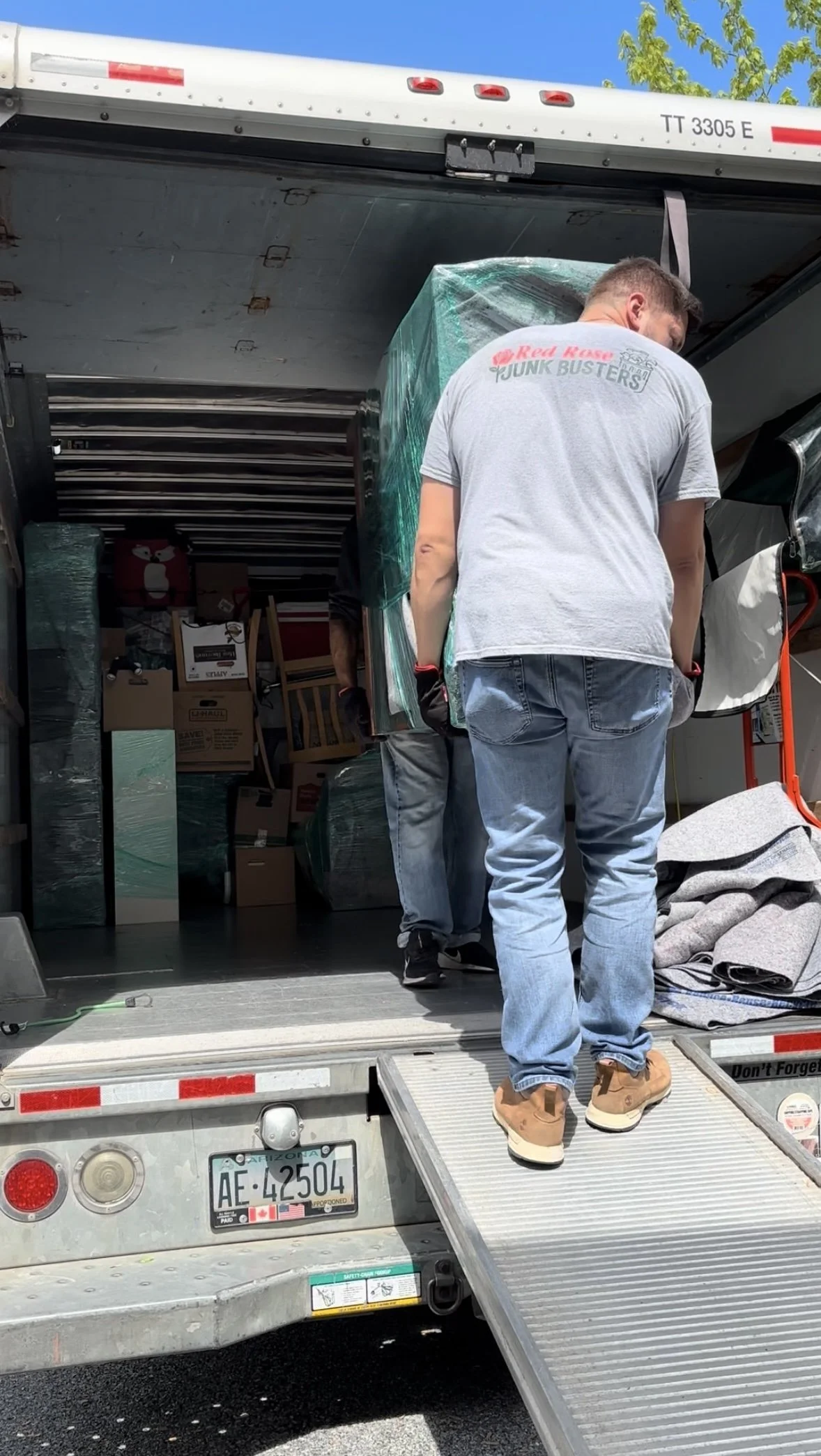 People unloading furniture and boxes from a moving truck on a sunny day.