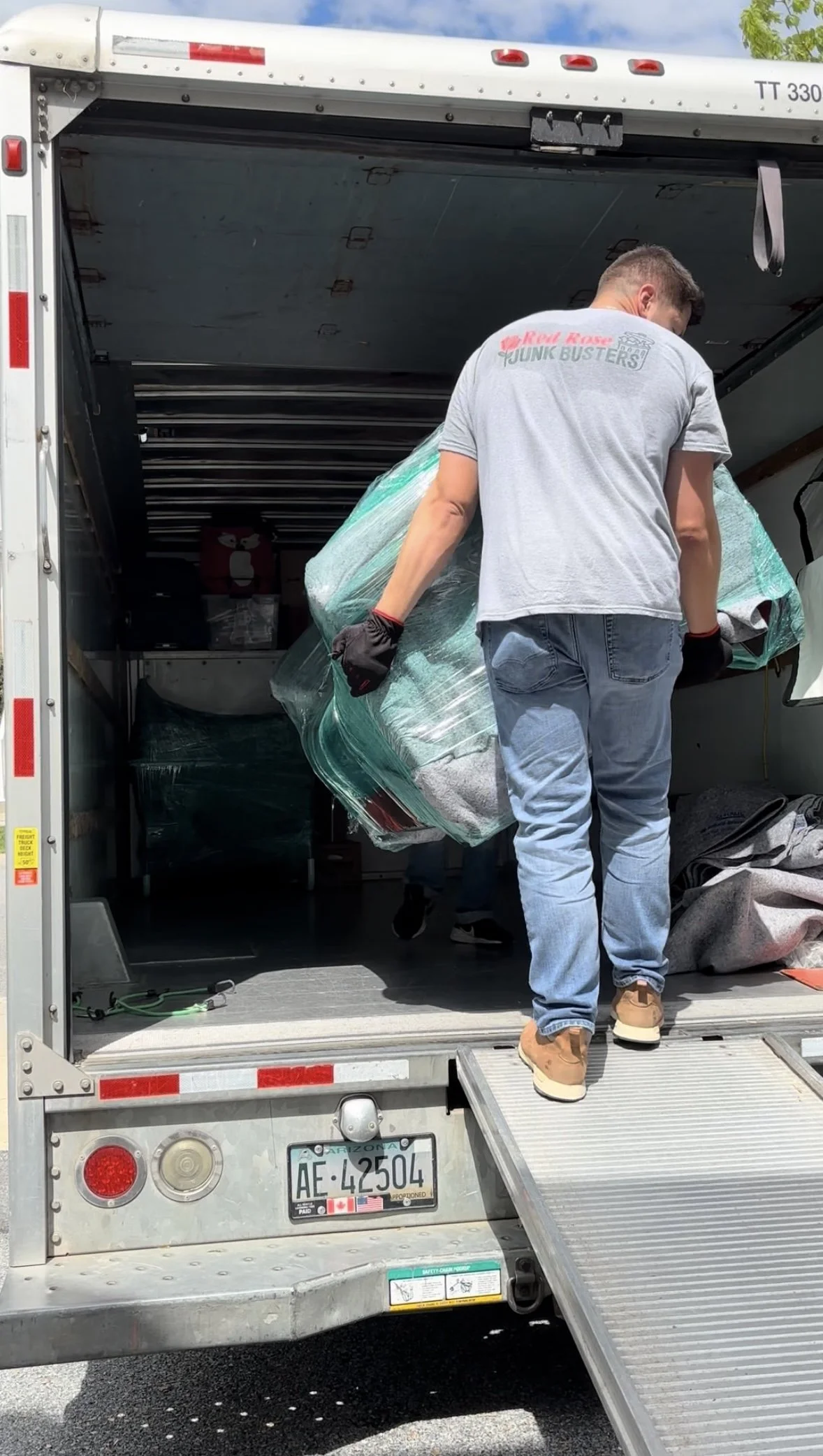 A man in a gray T-shirt and jeans loading a large wrapped item into a moving truck.