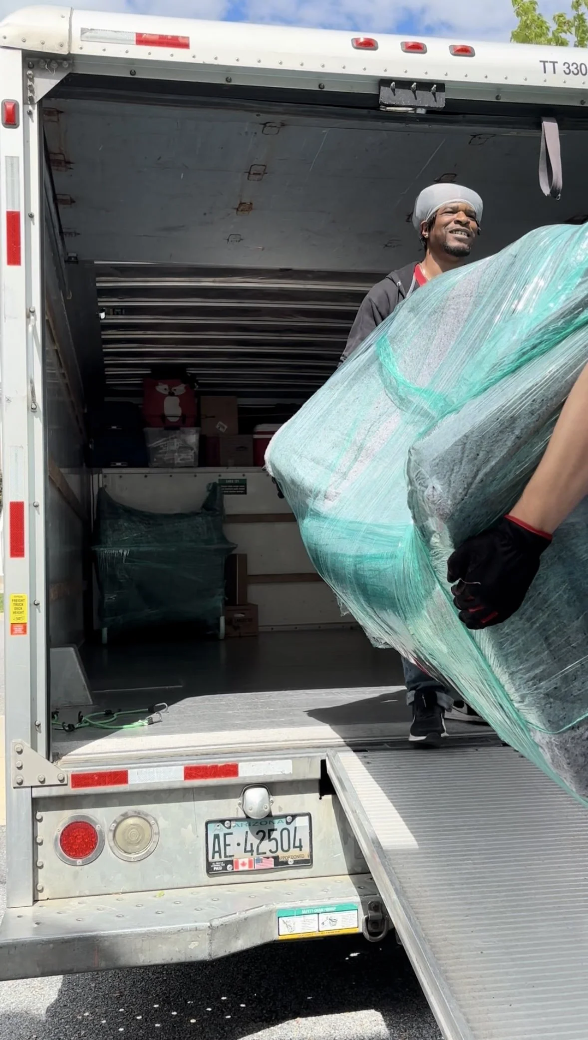 A man loading a wrapped, large item into a moving truck on a sunny day.