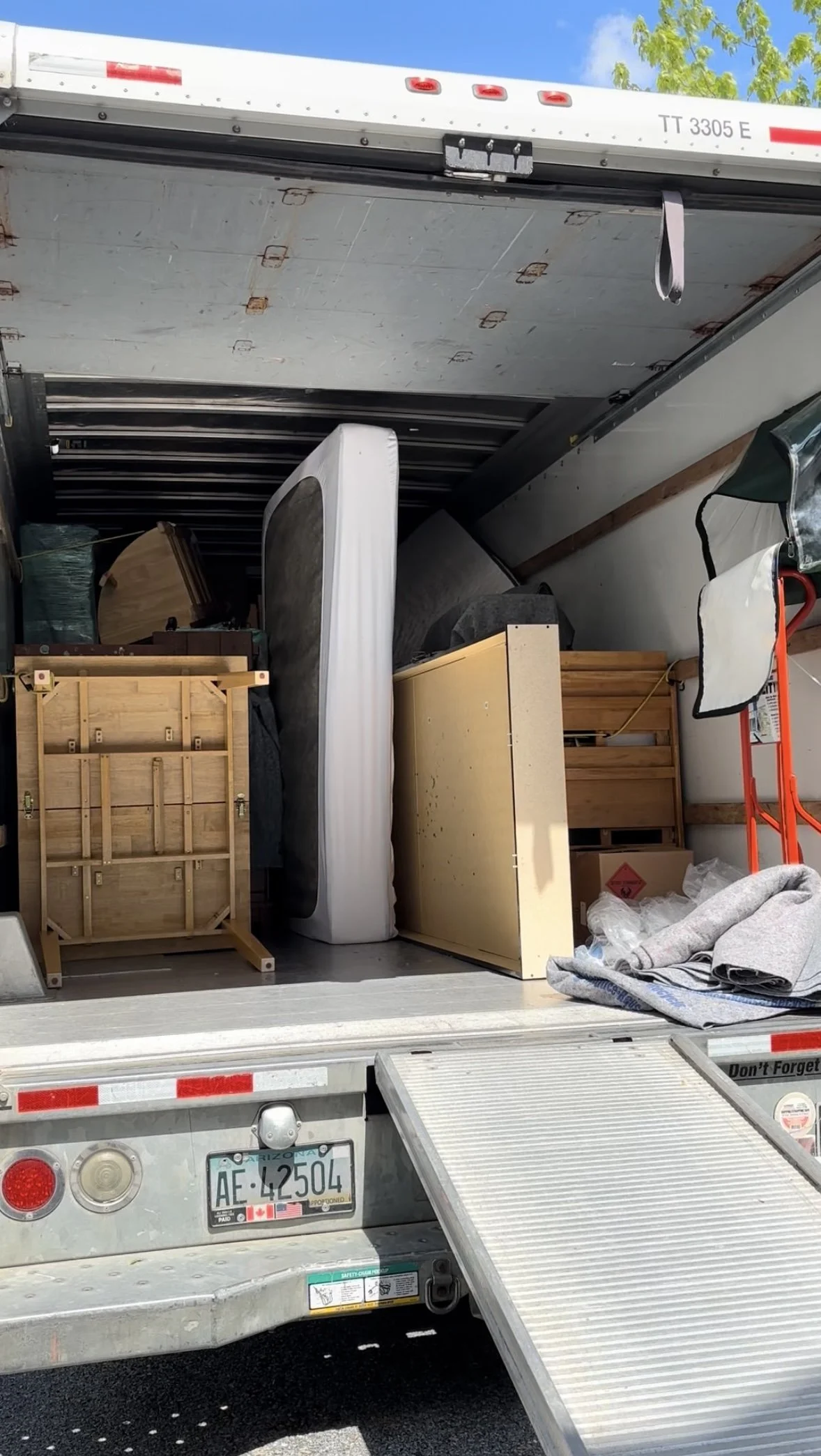 Open moving truck filled with furniture, boxes, and a folded ramp, with an Arizona license plate visible.