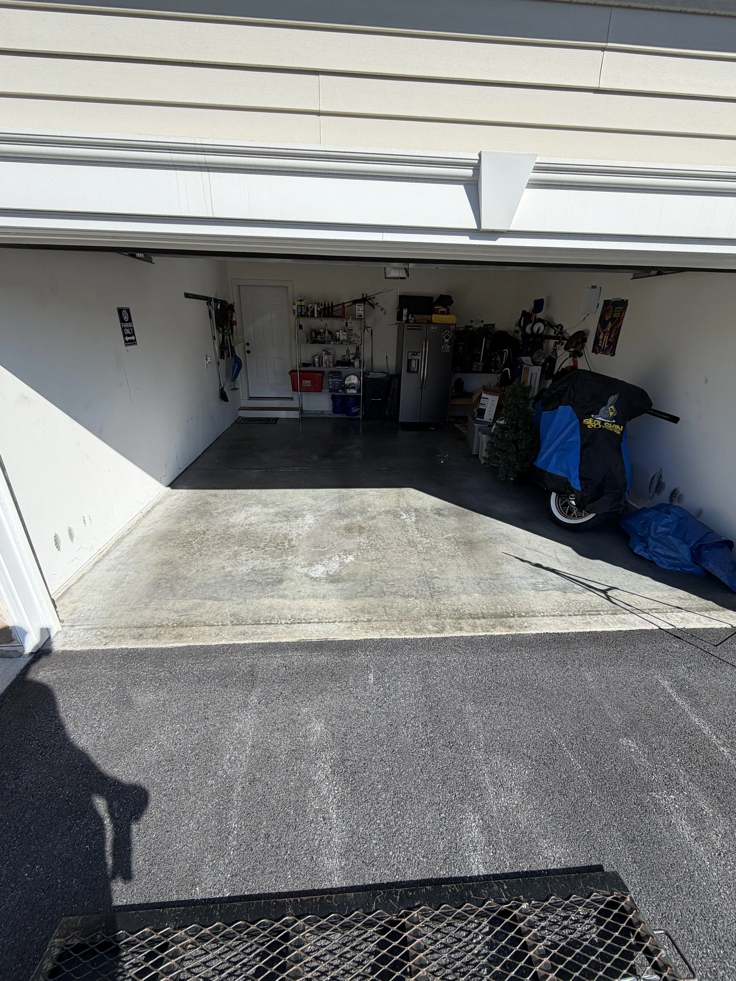 Open garage with tools, shelves, refrigerator, motorcycle covered with a blue tarp, and a small artificial Christmas tree inside.
