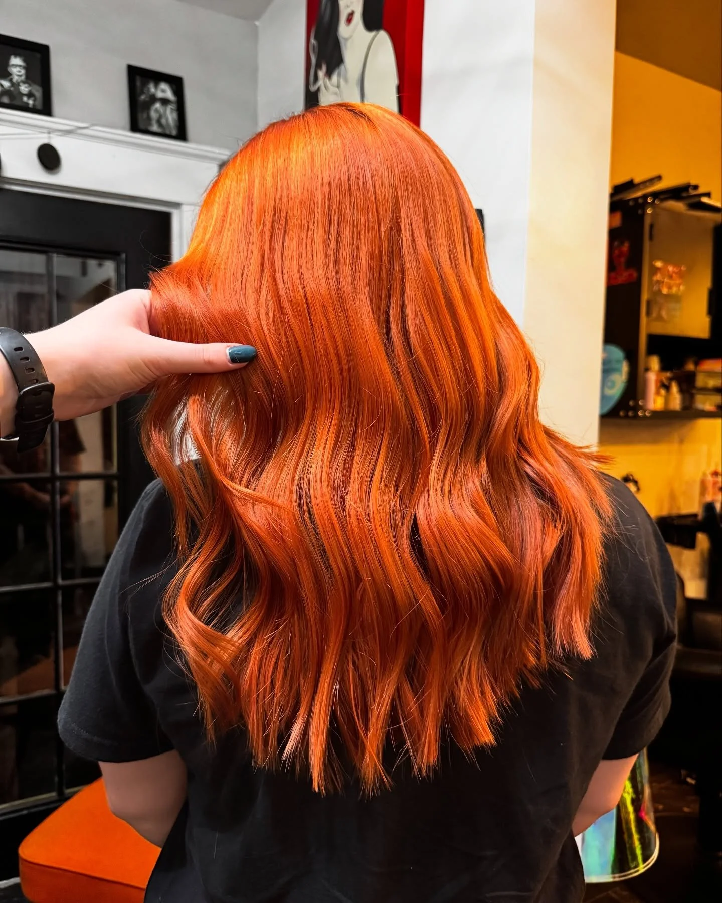 Back view of a person with long, wavy, bright orange hair inside a hair salon.