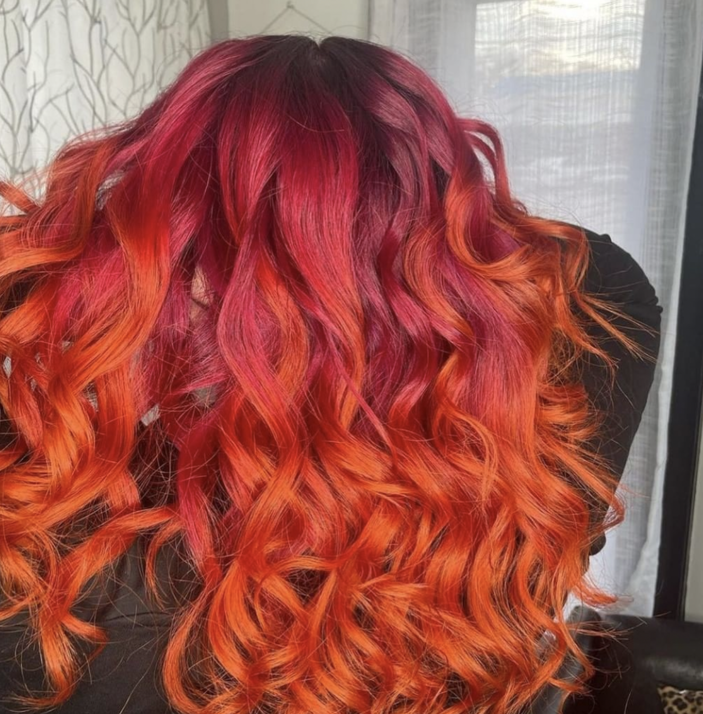 Woman with curly hair dyed in red, pink, and orange shades, draped over her face.