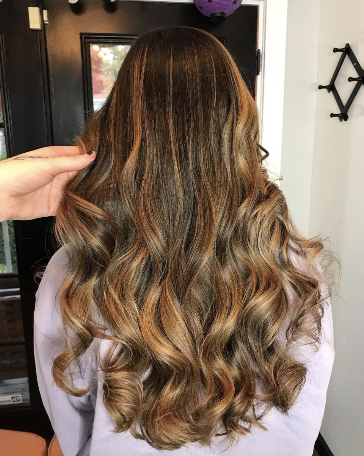 A person with long, wavy hair in shades of blonde and light brown, styled in loose curls.