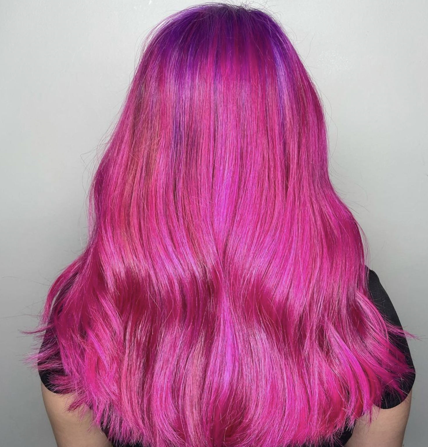 Back view of a person with long, wavy hair dyed in shades of pink and purple.