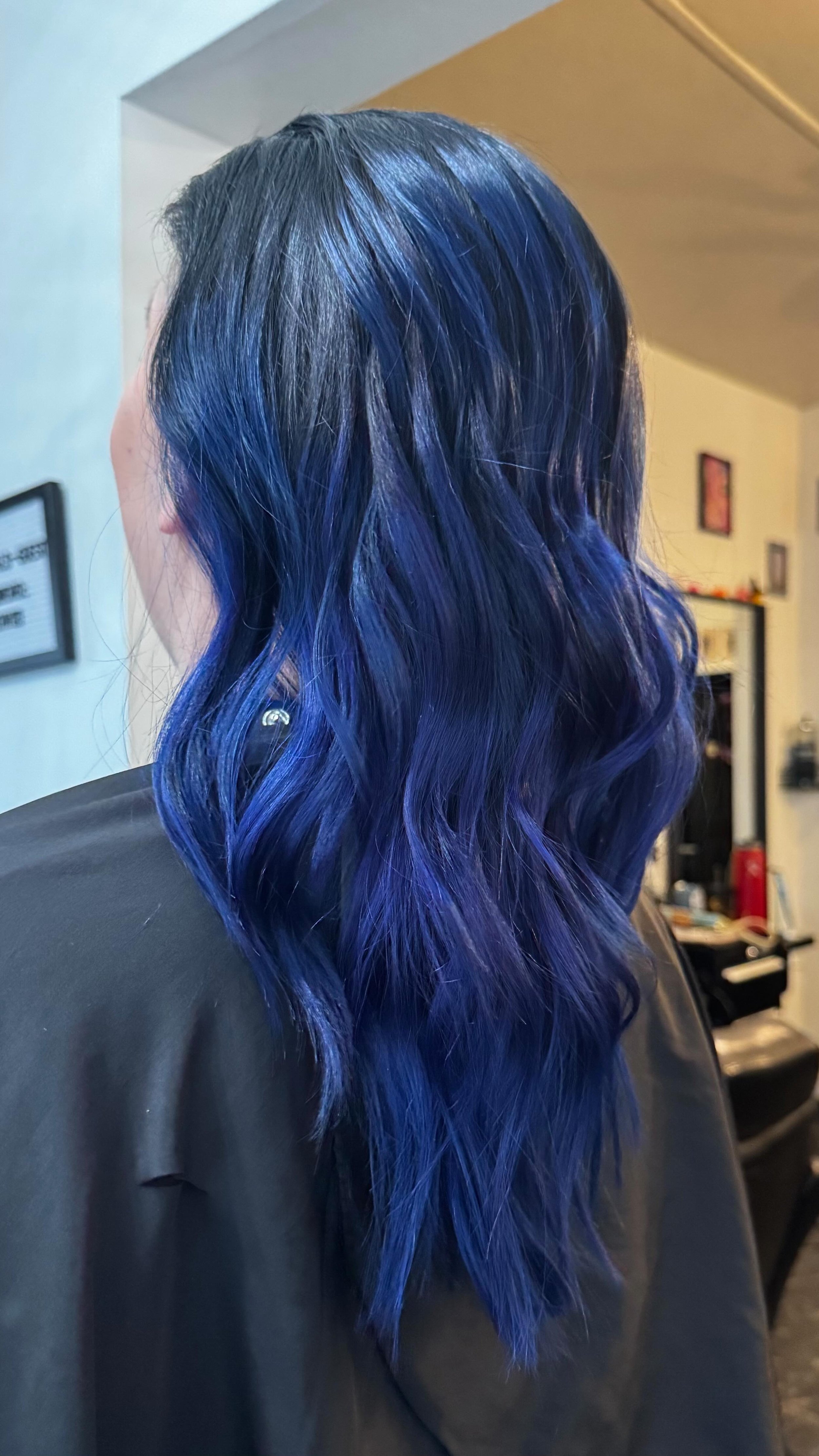 Person with long wavy hair dyed in vibrant blue shades, sitting in a salon chair.
