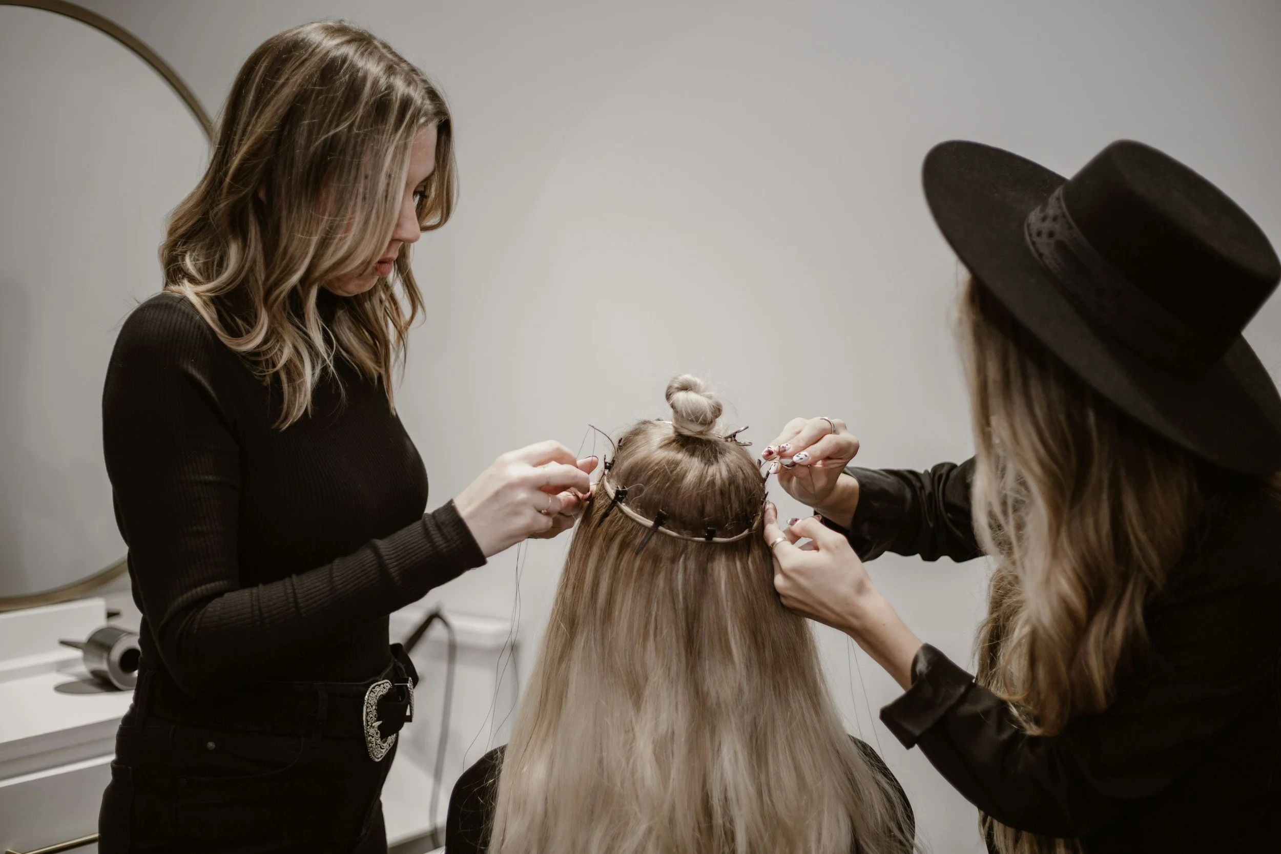 Two hairstylists working on a client's hair, creating a hairstyle with clips and accessories, in a salon setting.