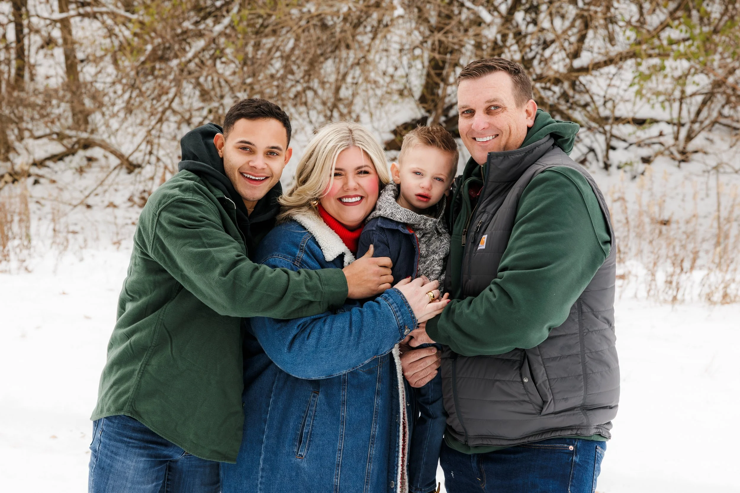 A family of five standing outdoors in a snowy landscape, smiling and posing for a photo, dressed in winter clothing.