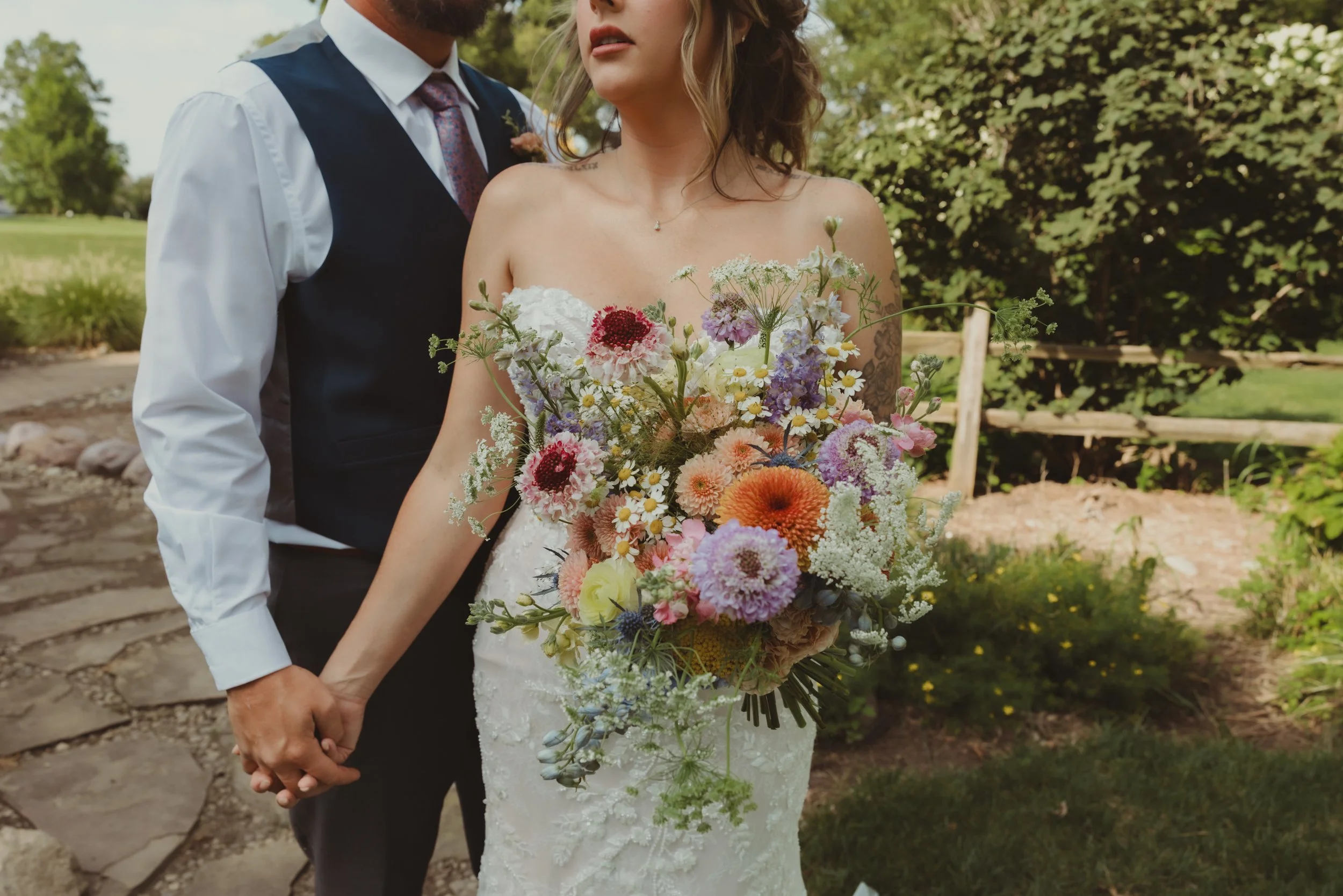 A bride and groom holding hands outdoors, with the bride holding a large bouquet of colorful flowers.