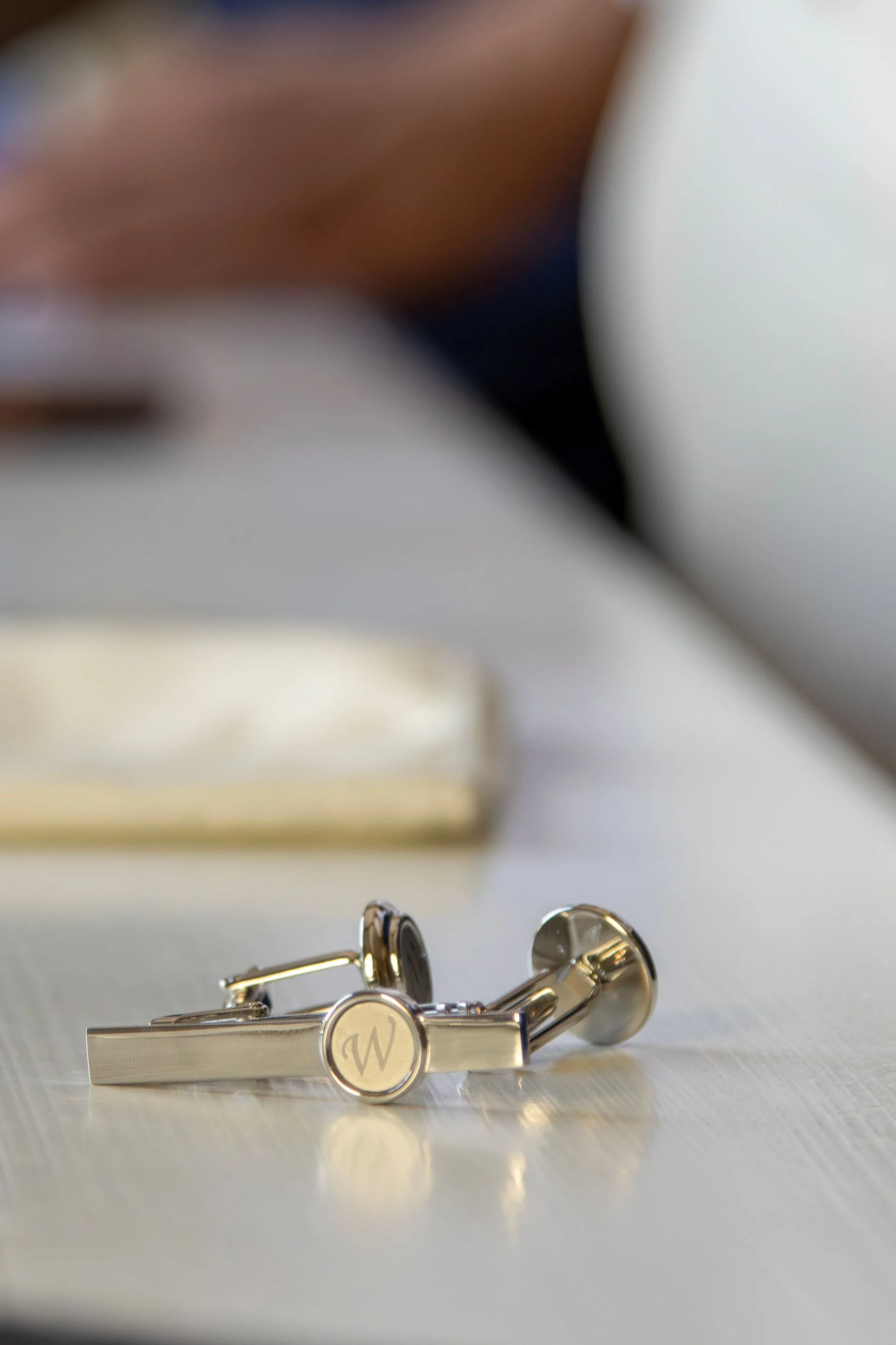 Close-up of gold cufflinks with a monogrammed letter 'W' on a white surface.